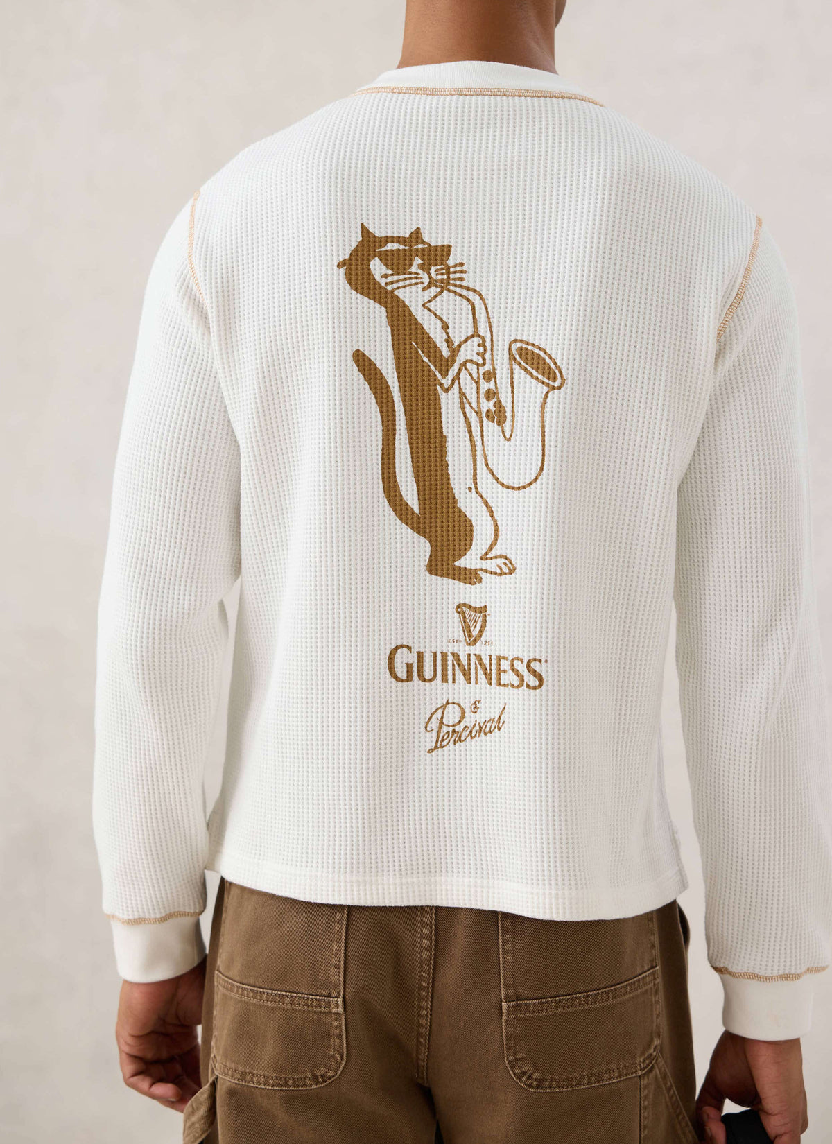 Rear view of a model wearing the cream waffle henley from Guinness x Percival, featuring the illustrated jazz cat graphic.