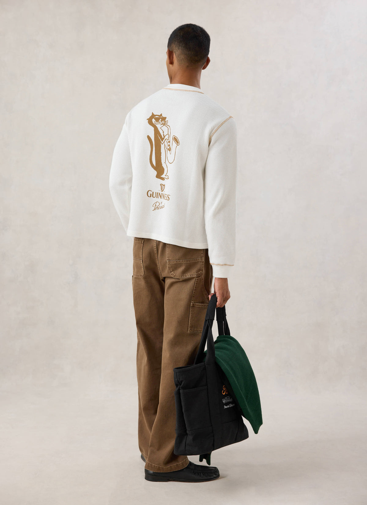 Rear view of a model wearing the Guinness x Percival cream waffle henley long sleeve t-shirt, showing the back cat graphic.