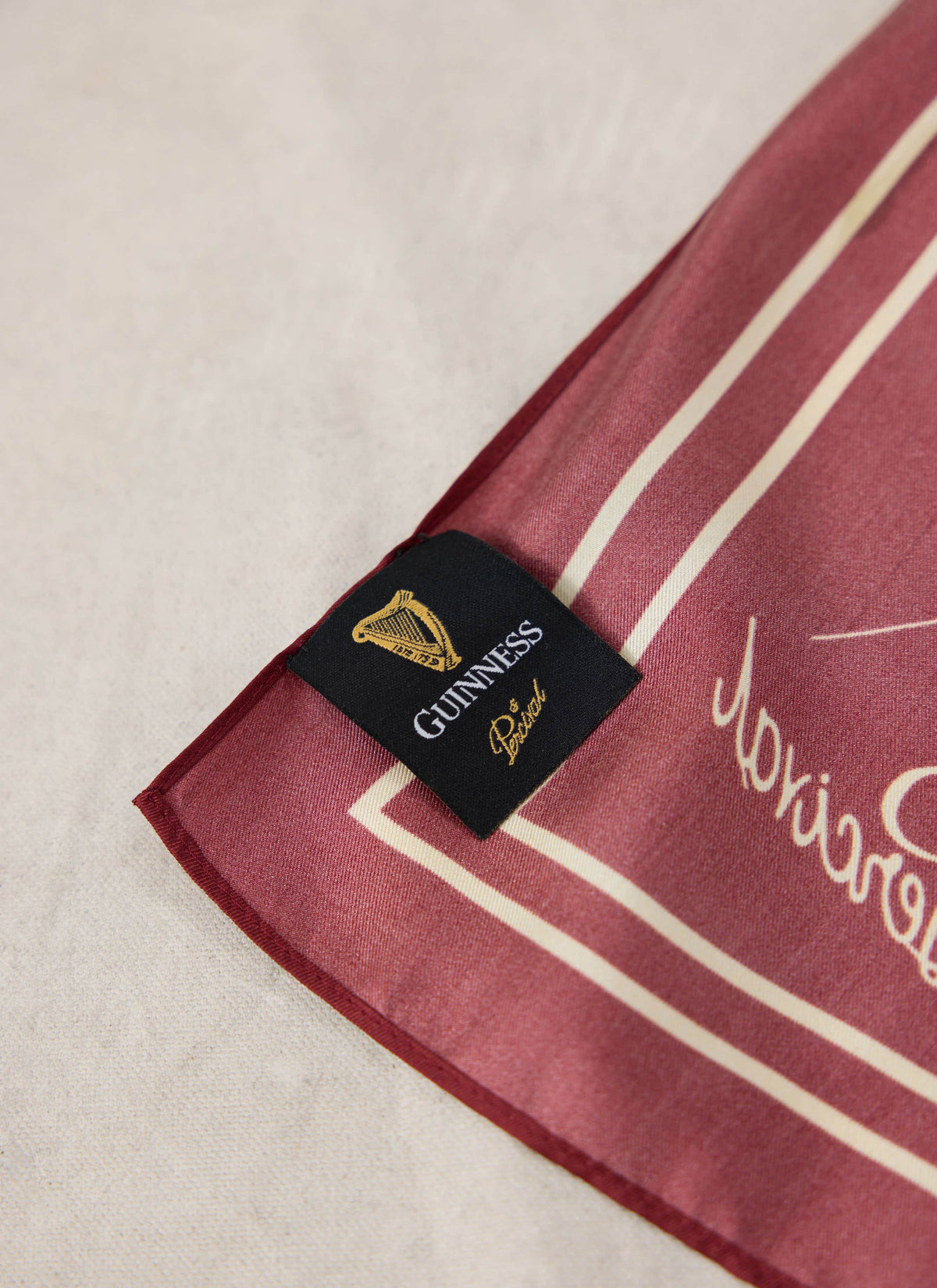 Close-up of the burgundy Guinness x Percival neckerchief, showing the woven label and contrast border.