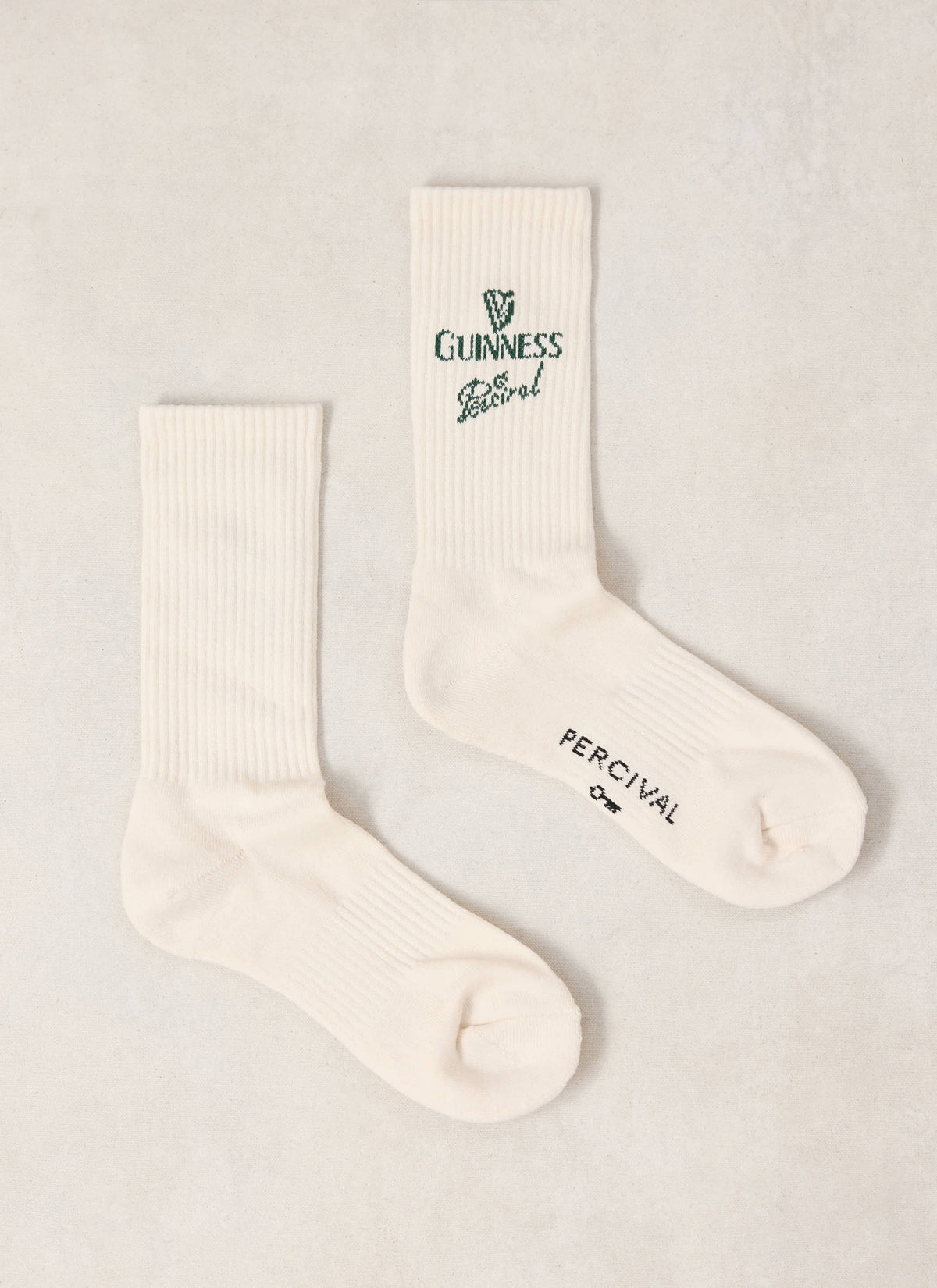 Pair of Guinness x Percival cream ribbed crew socks featuring green branding and text details.