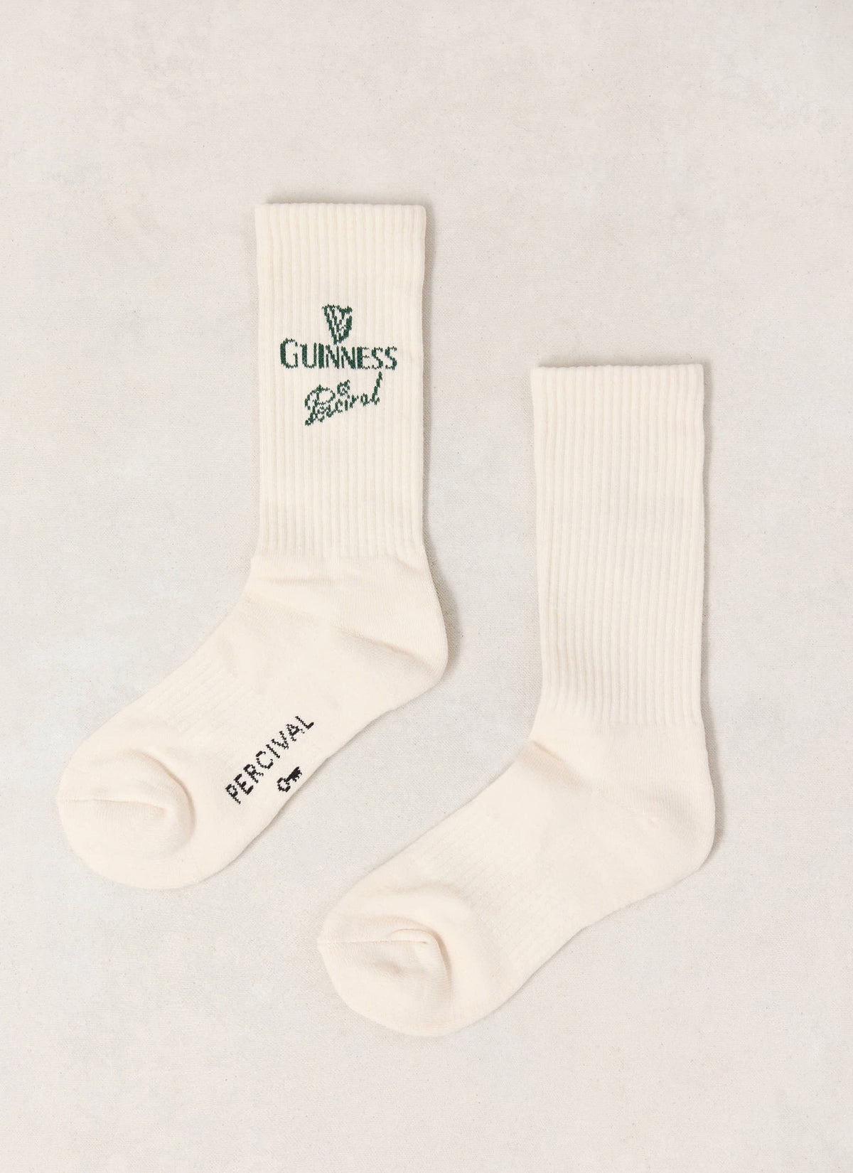 A pair of cream Guinness x Percival ribbed crew socks featuring green co-branded logo detailing.