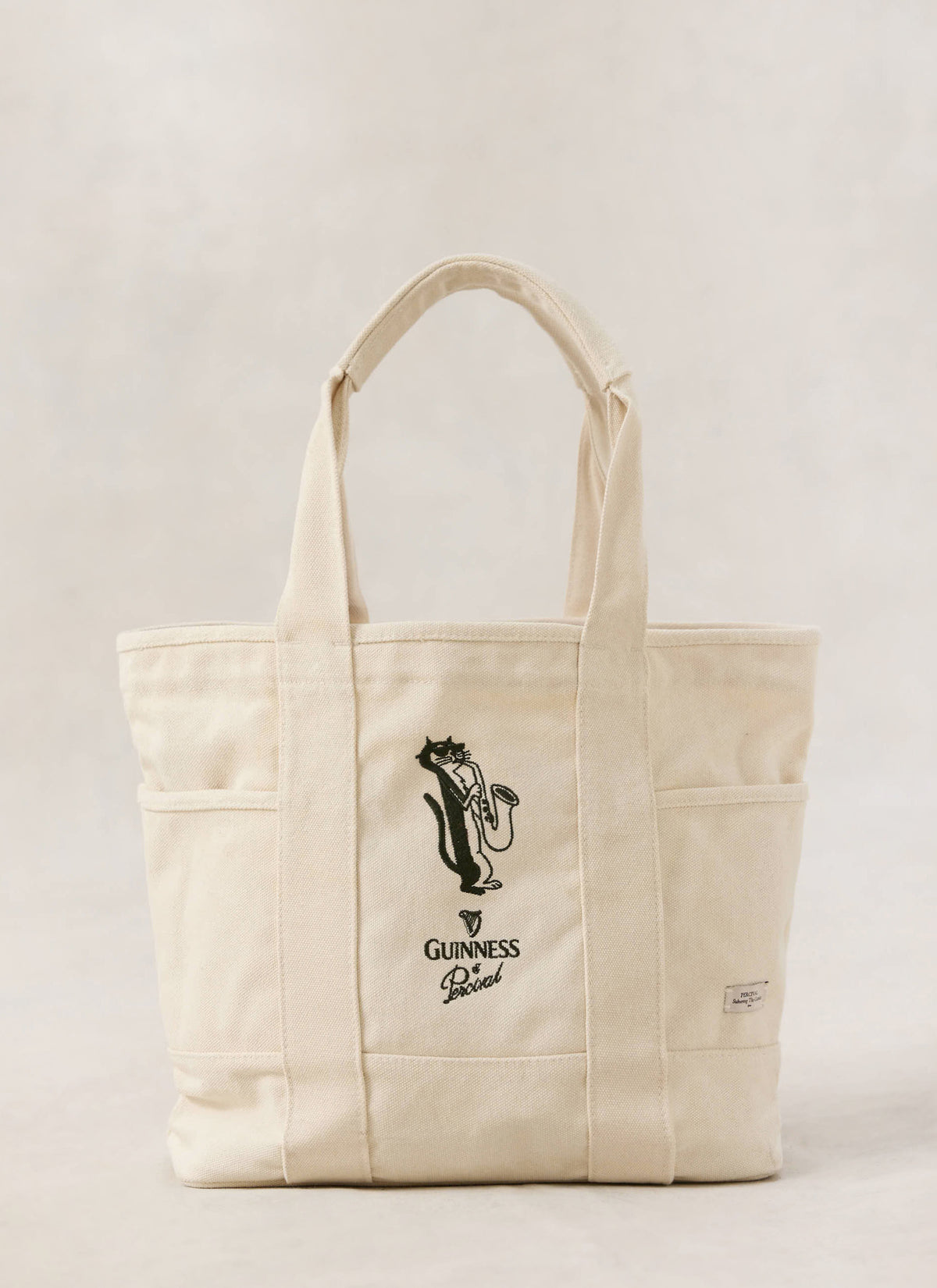 Cream Guinness x Percival tote bag featuring the embroidered saxophonist cat artwork and branding on the front.