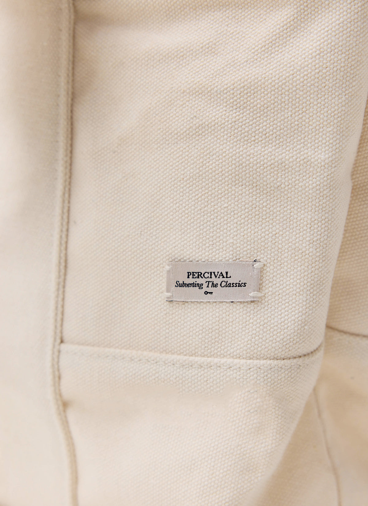 Close-up of the cream Guinness x Percival tote bag showing the branded woven label and textured fabric.
