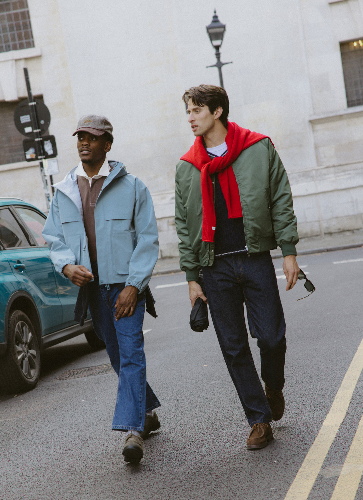 Two models walking outdoors, one wearing a green bomber with the red roll-neck jumper tied around his shoulders.
