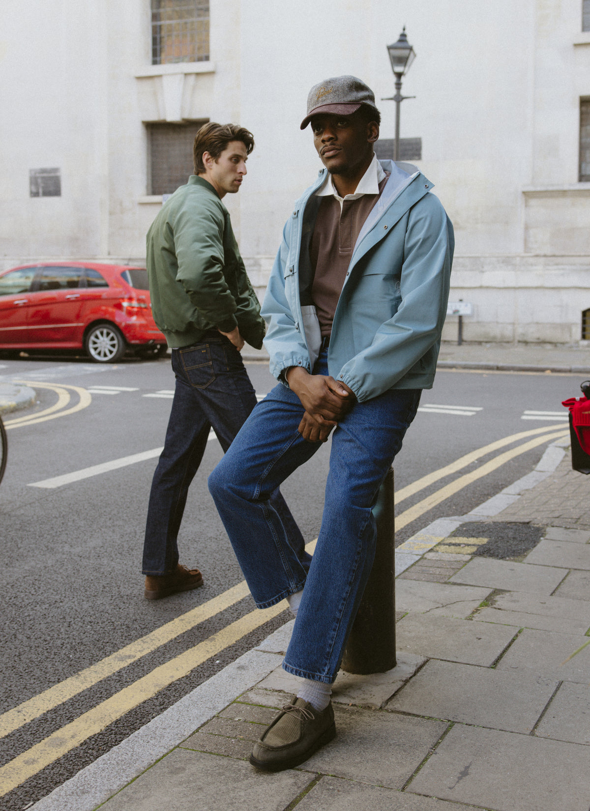 Two models outdoors on a street, with the foreground model wearing the brown Editor rugby polo shirt and a light blue jacket.