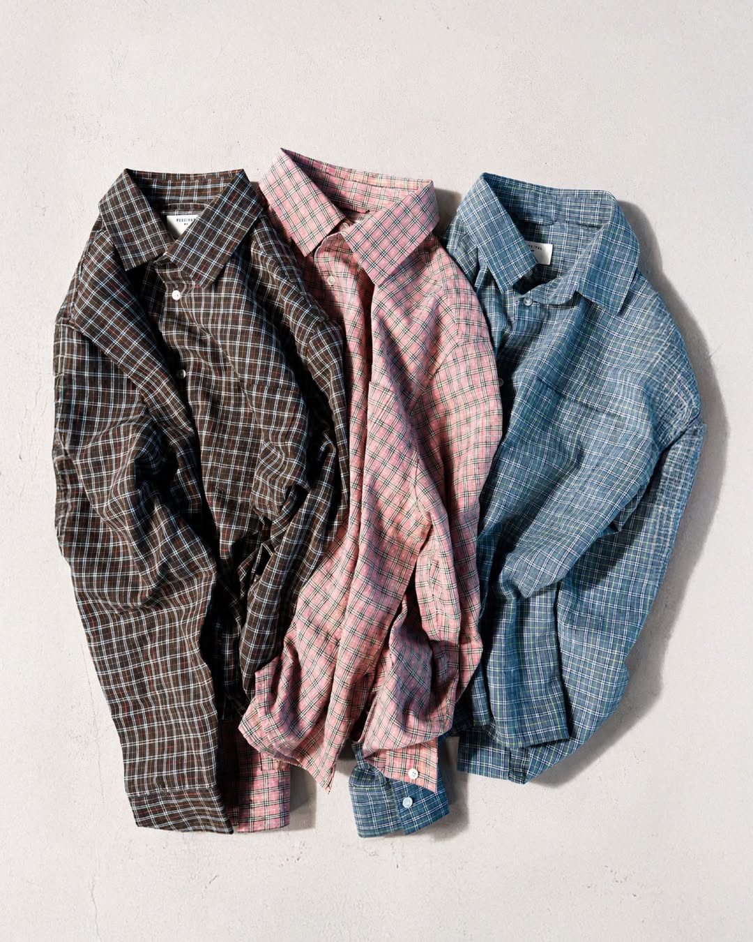 Percival Hinsley checked boxy shirts in brown, pink, and blue cotton, shown together against a light textured wall.