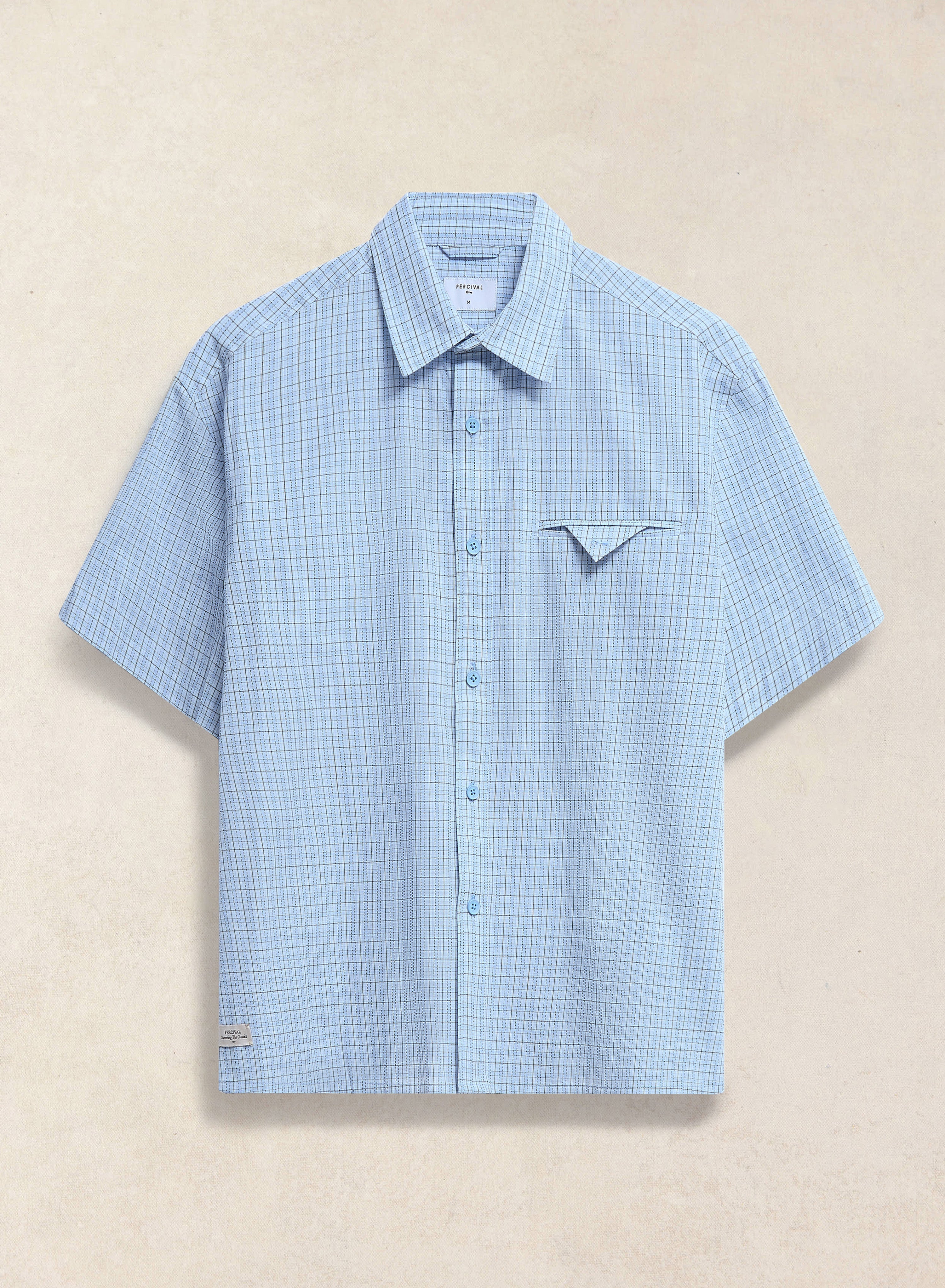 The Percival Hinsley boxy short sleeve shirt in blue check cotton, featuring a unique geometric chest pocket detail.