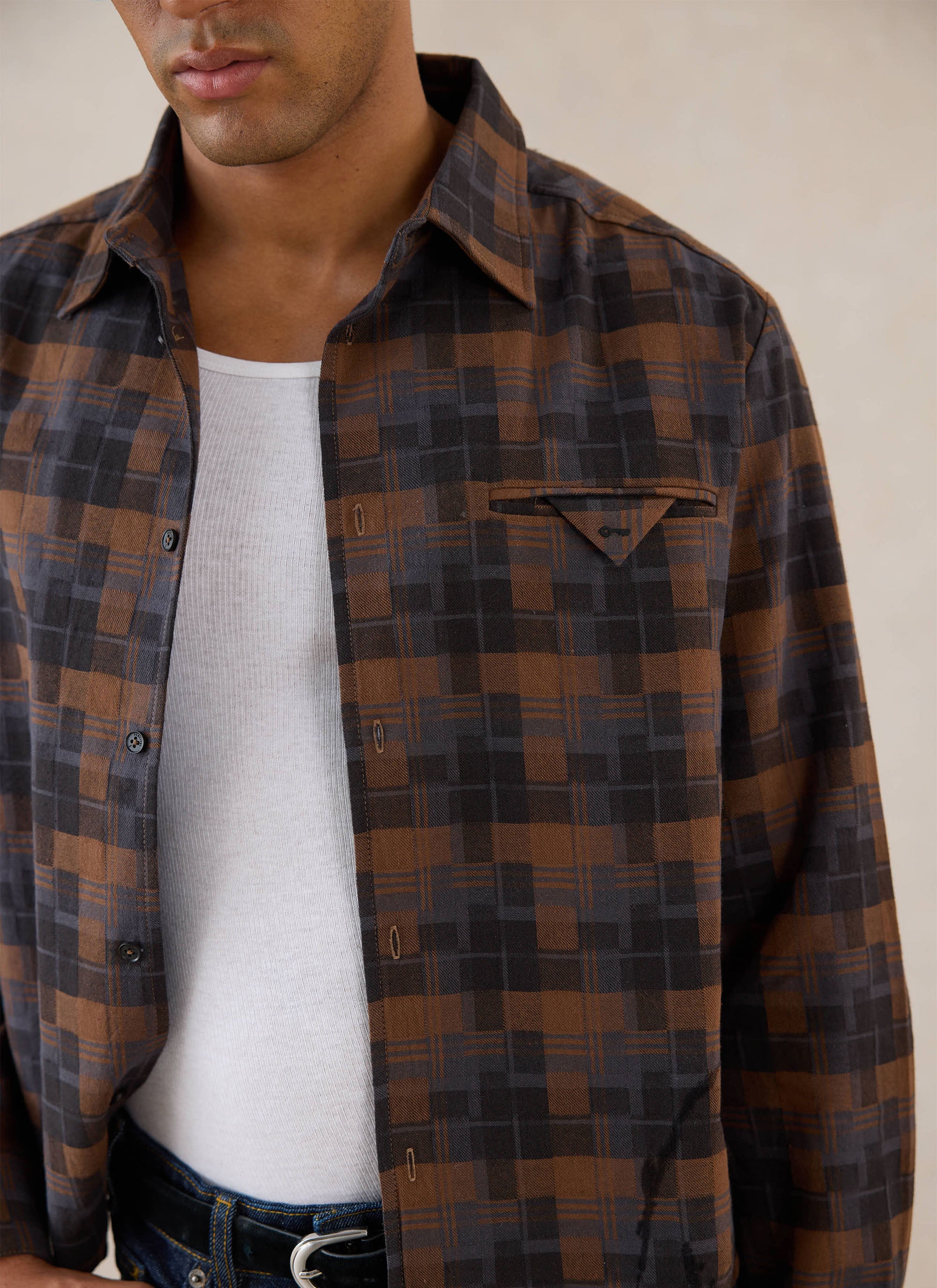A close-up of a model wearing the brown check Percival Hinsley shirt over a white vest.
