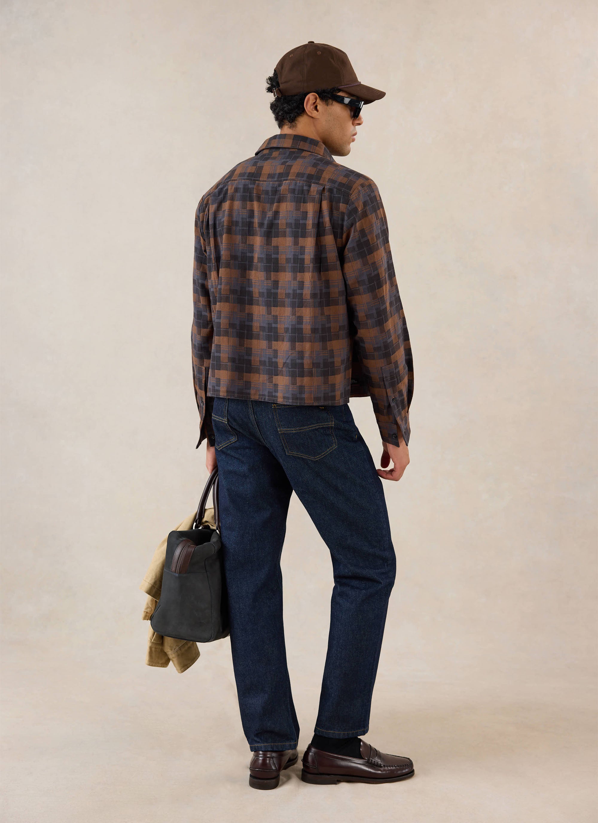 A model seen from behind wears the brown check Hinsley boxy long sleeve shirt from Percival with dark jeans and loafers.