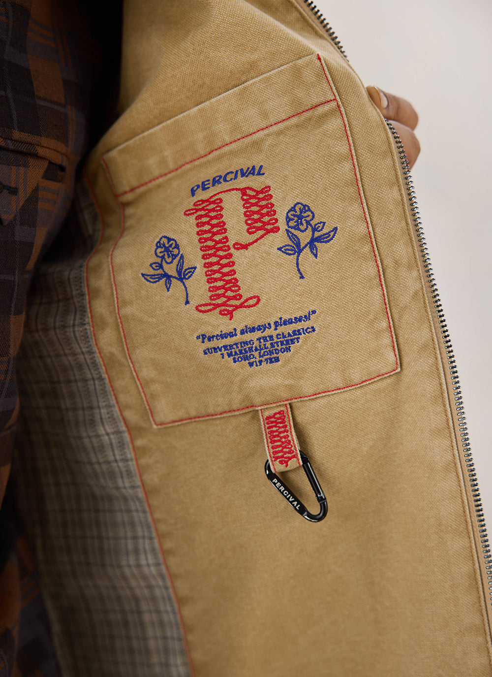 A close-up view of the interior embroidered pocket and carabiner detail on the cream Jackson Harrington Jacket from Percival.