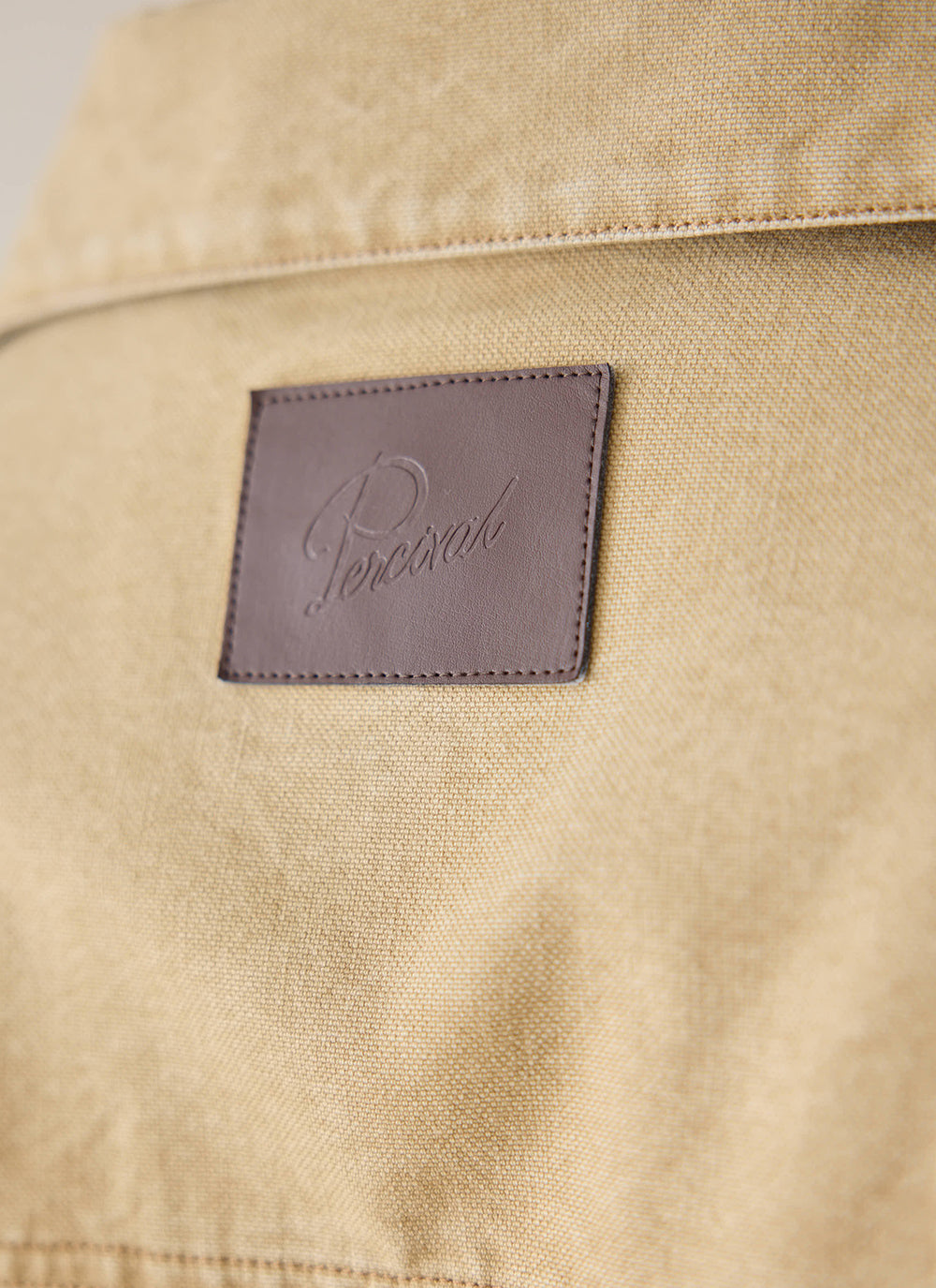 A close-up of the cream Percival Jackson Harrington Jacket, showing the branded leather patch detail.