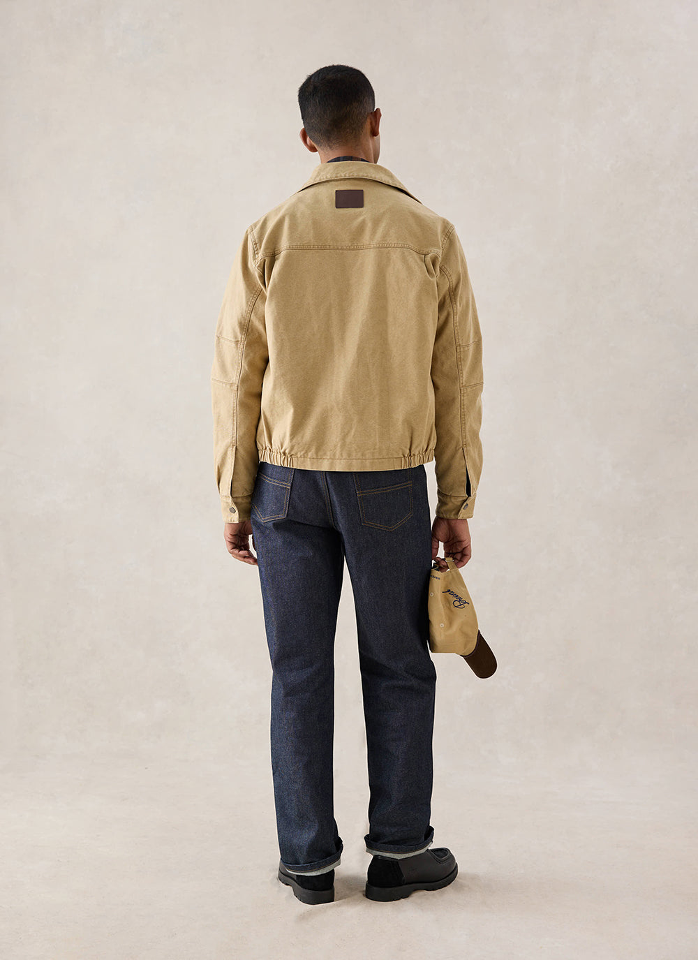 A rear-view shot of a model wearing the cream Jackson Boxy Harrington Jacket from Percival, styled with dark jeans.
