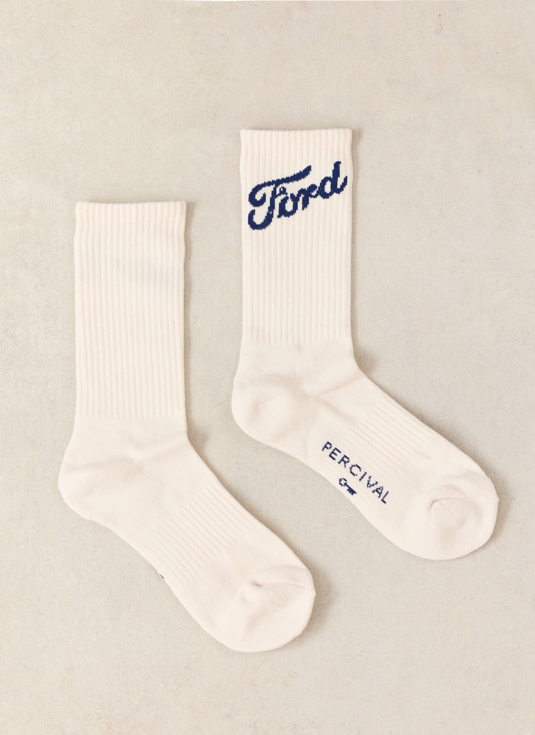 Cream ribbed Ford x Percival jacquard crew socks featuring navy blue branding and a signature key graphic.