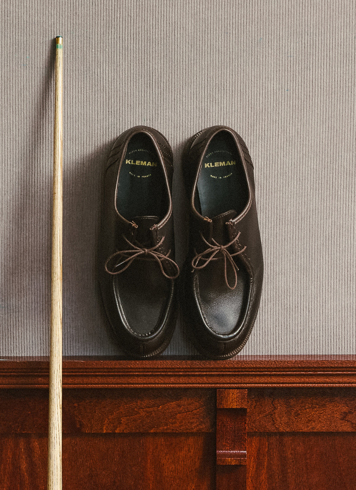 A pair of brown Kleman shoes showcased on a wooden ledge alongside a pool cue, styled for Percival.