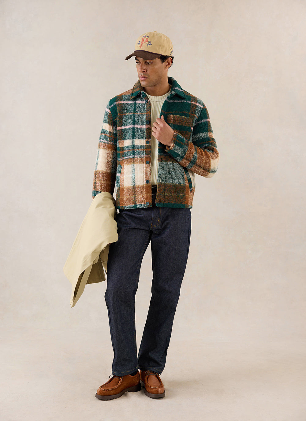 A model wears the Percival Knowles Overshirt in multi check, styled with dark jeans, brown shoes and a cap in a studio.