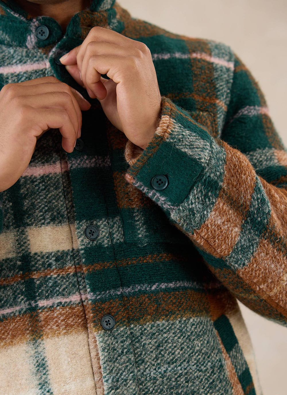 A close-up of a model fastening the buttons on the multi check wool Knowles overshirt from Percival.