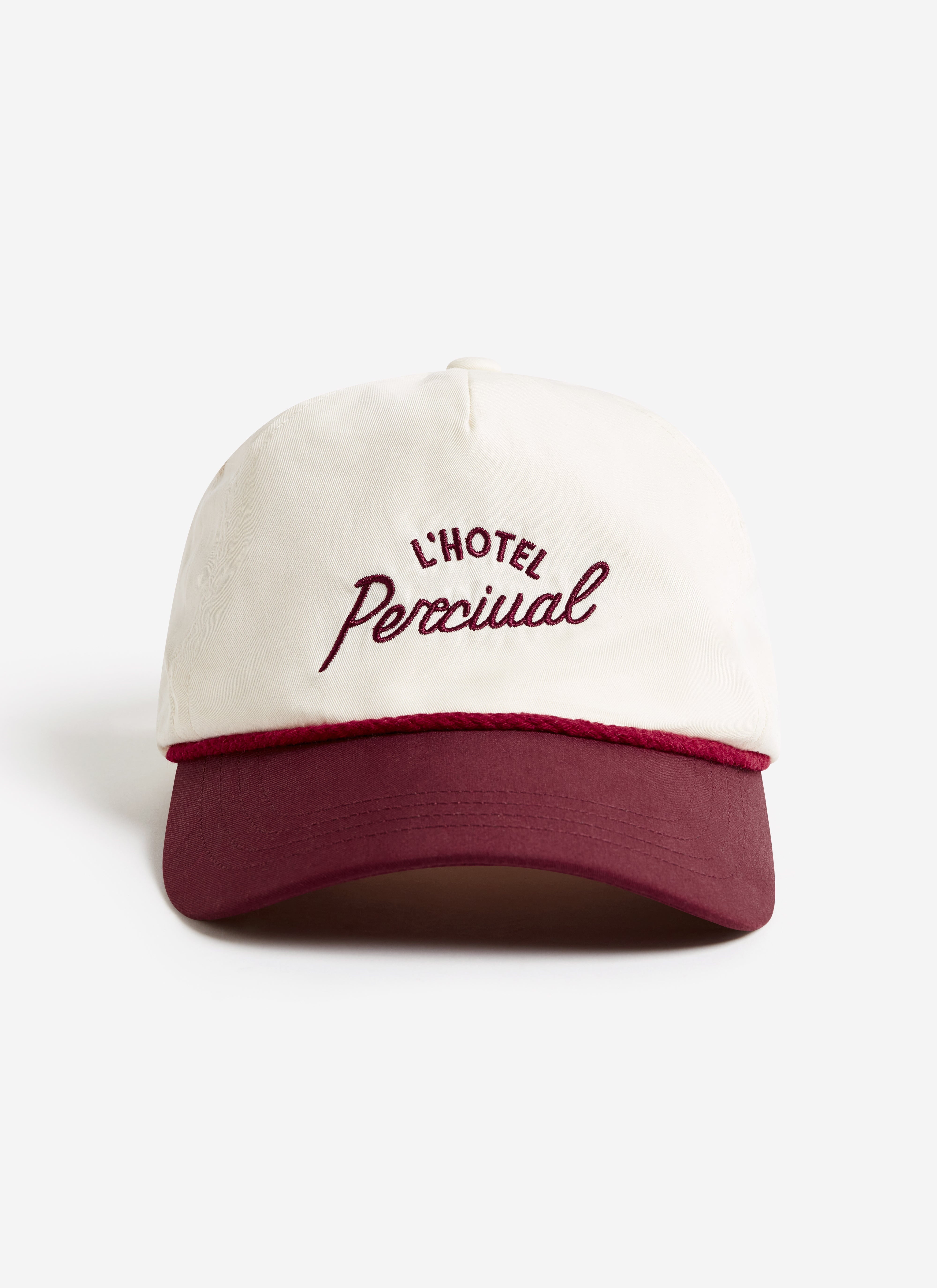 A studio photograph of the L'Hotel Percival soft trucker cap in ecru, with burgundy embroidery and peak.