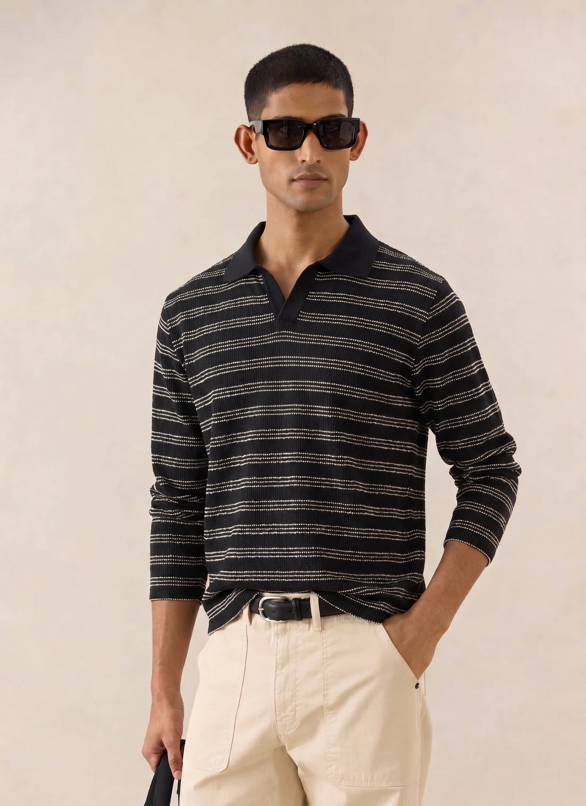 A model wearing the black striped Percival Laurent Long Sleeve Polo with light trousers and sunglasses.