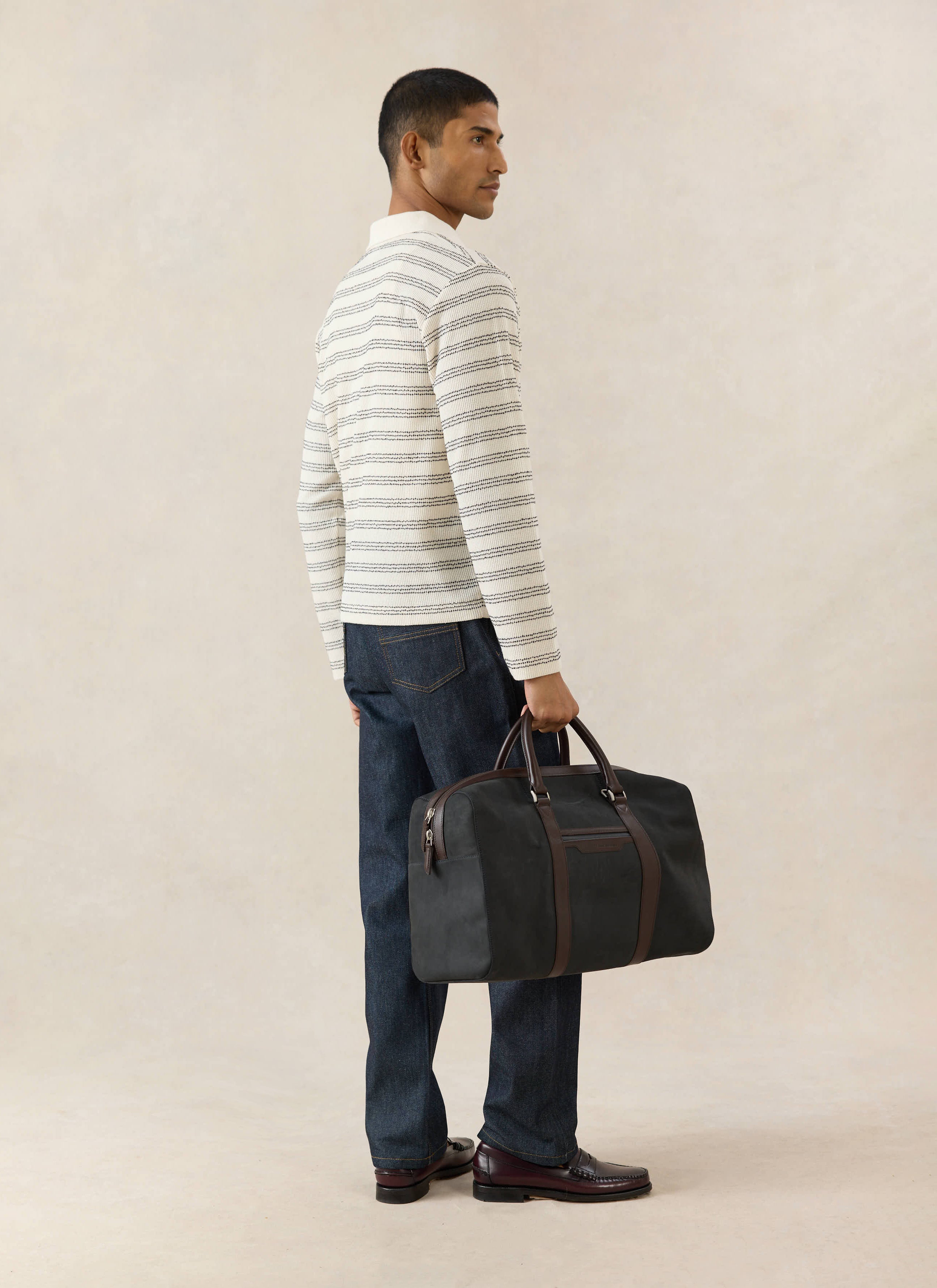 Percival Laurent long sleeve cream polo in a textured cotton blend, worn with dark denim jeans and a holdall bag.