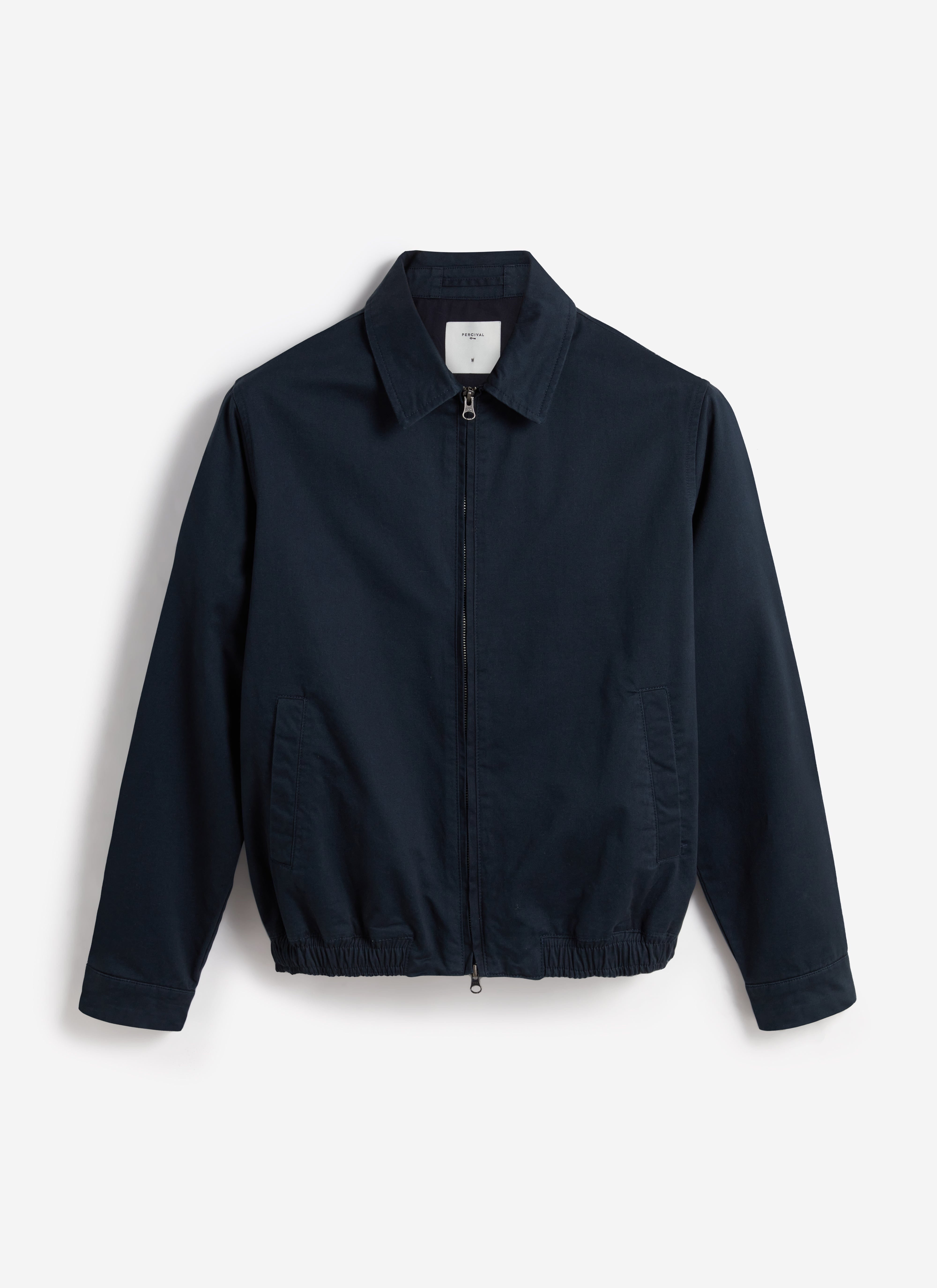A flat lay of the Percival Leo Harrington Jacket in navy cotton, showing the front view with its classic collar and zip.