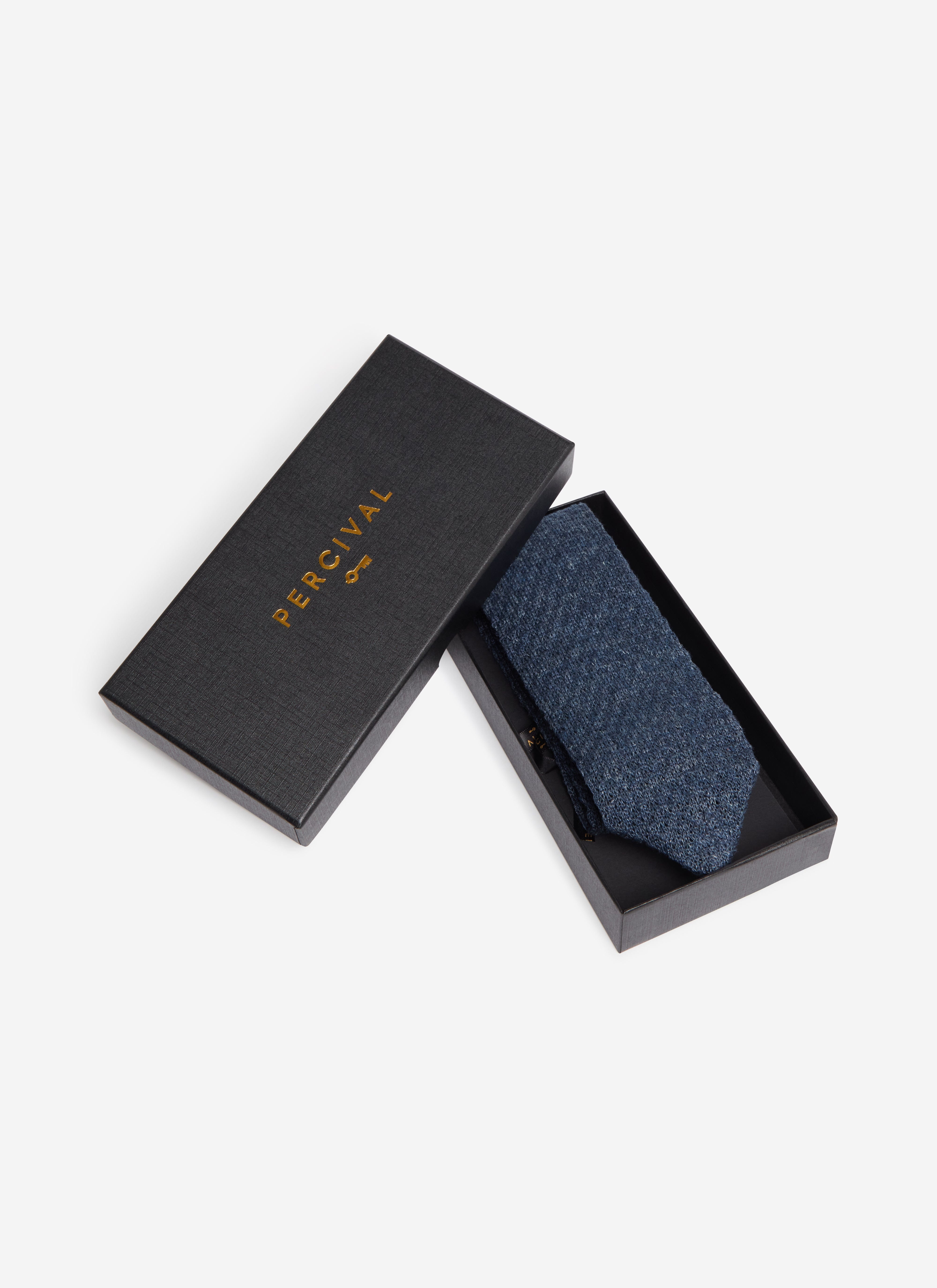 A studio shot of the Percival Linen Tie in navy marl, folded and presented in its black branded gift box.