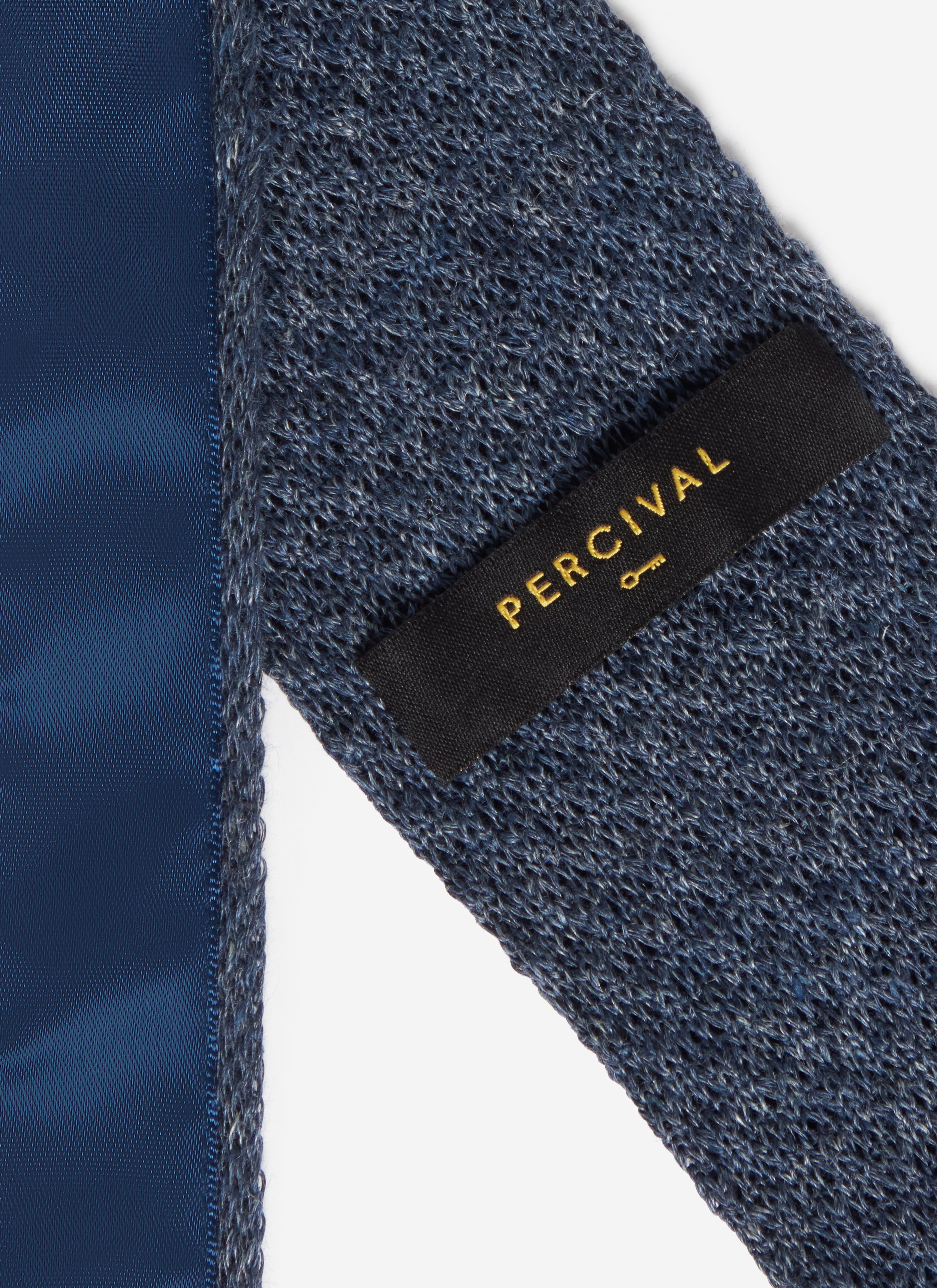A close-up of the reverse of the Percival Linen Tie in navy marl, showing the branded label and textured knit.