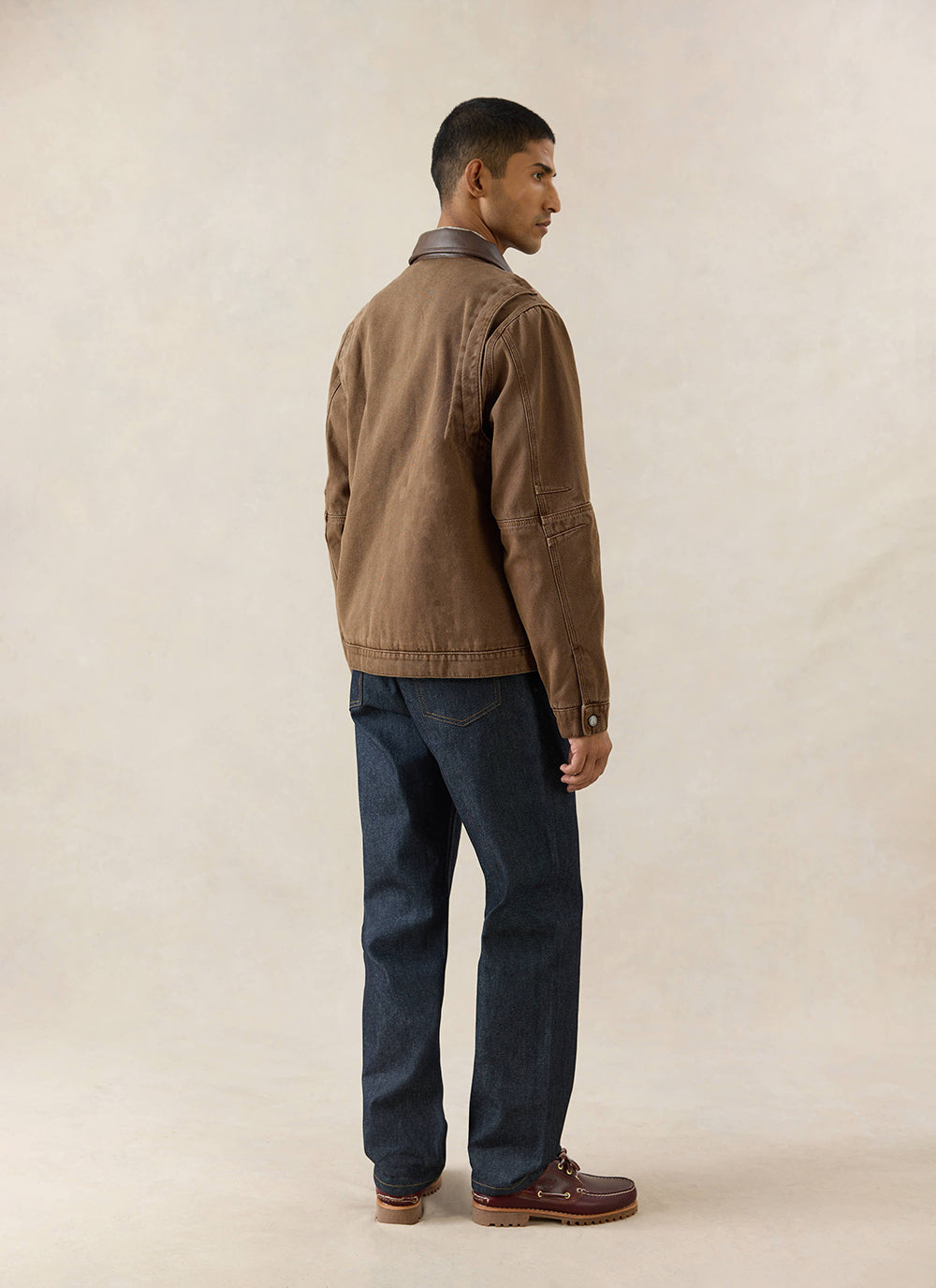 A model wears the mocha Lucas Contrast Collar Jacket from Percival, styled from the back with dark denim jeans.