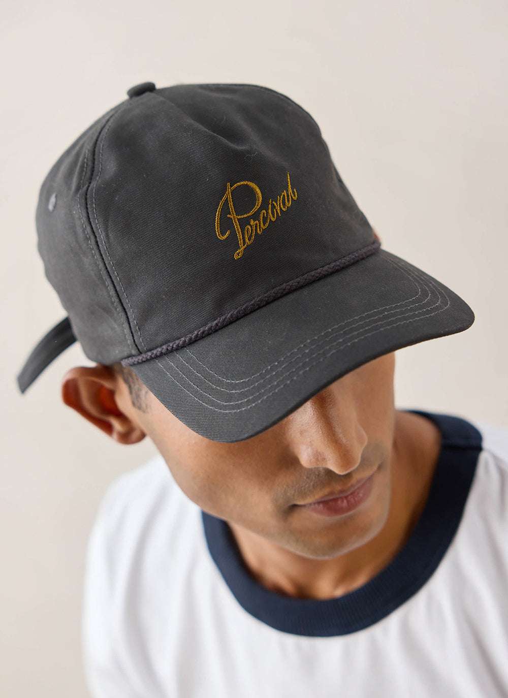 Close-up of a model wearing the charcoal Luther soft trucker cap by Percival, showing the embroidered logo.