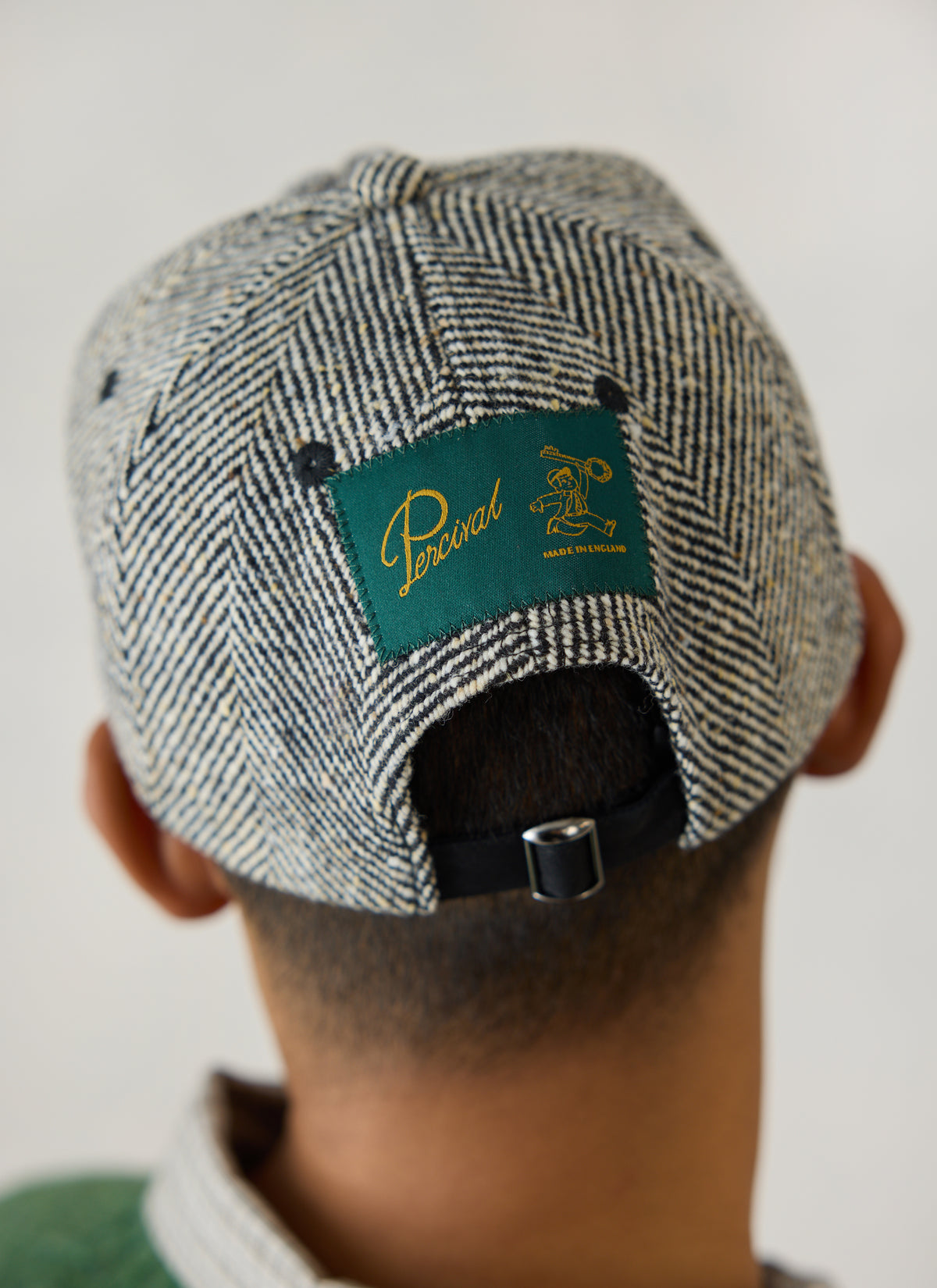 The back of the Percival grey herringbone wool cap, showing the green Made in England label and adjustable strap.