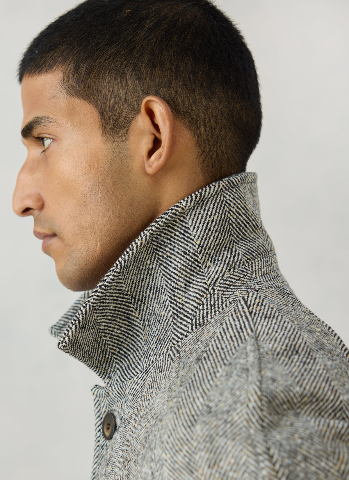 A profile close-up of a model wearing Percival's grey herringbone wool car coat, highlighting the raised collar detail.