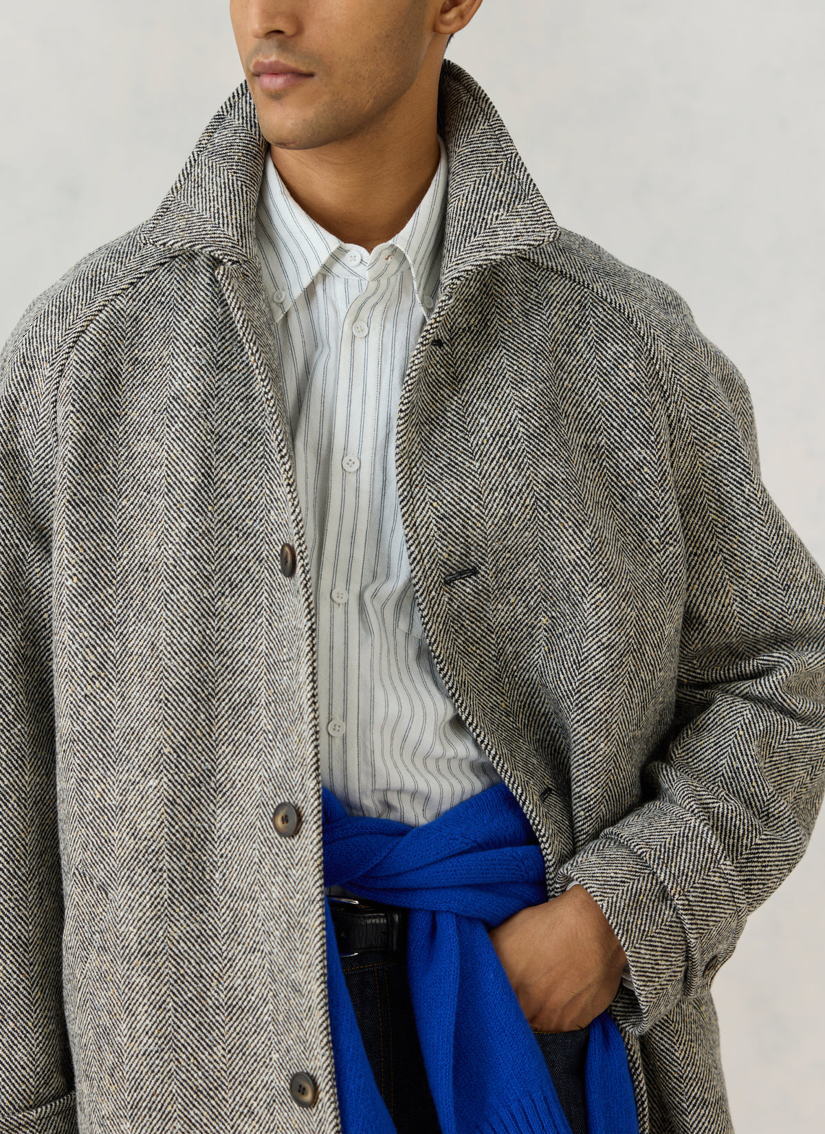 A model wearing the grey herringbone wool car coat by Percival over a striped shirt and a blue jumper.