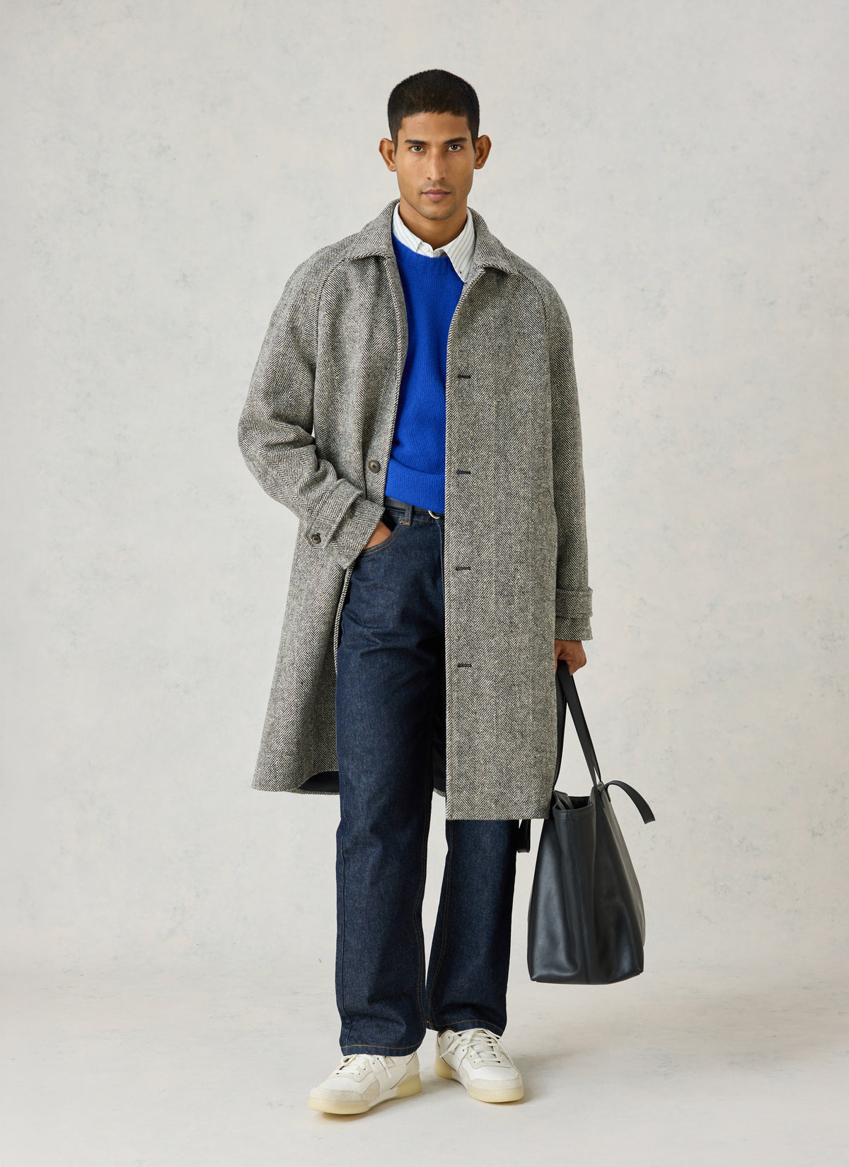 A model wearing the Percival grey herringbone wool car coat over a blue jumper and jeans, holding a leather tote bag.
