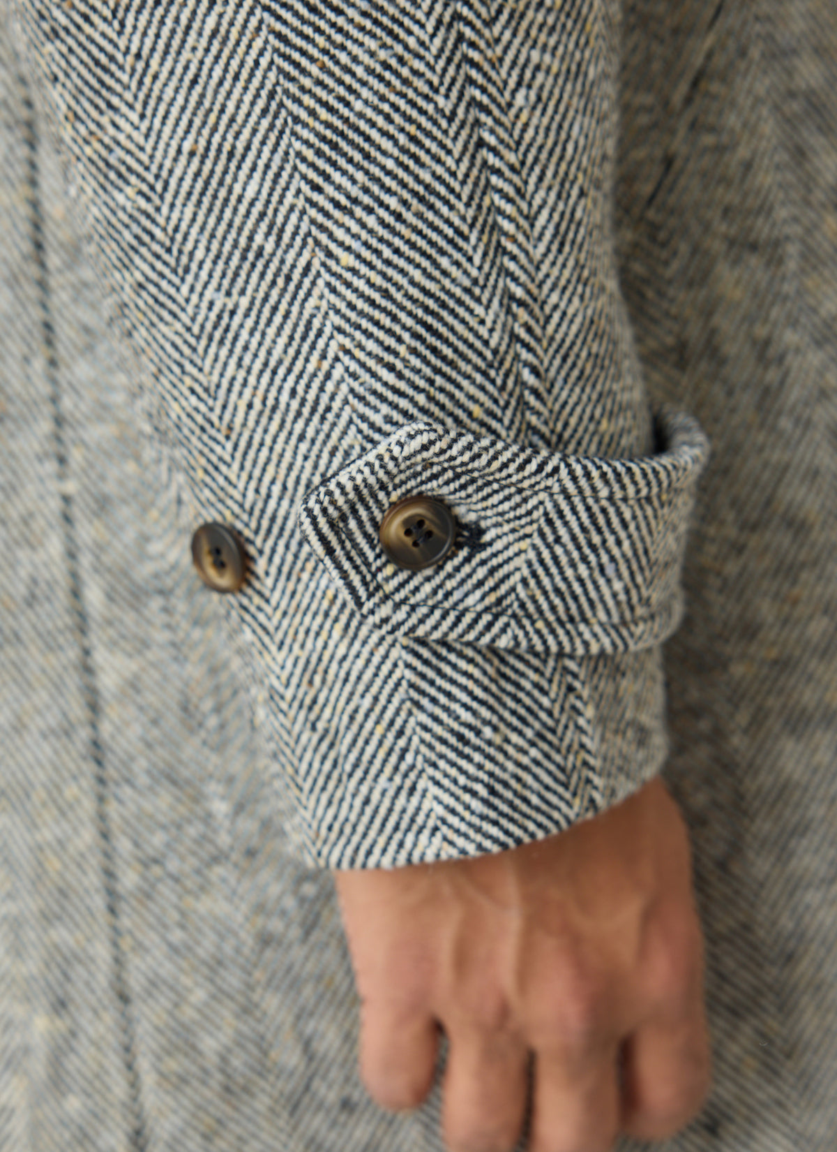 A close-up of the grey herringbone wool car coat cuff, showcasing the buttoned cuff tab detail.