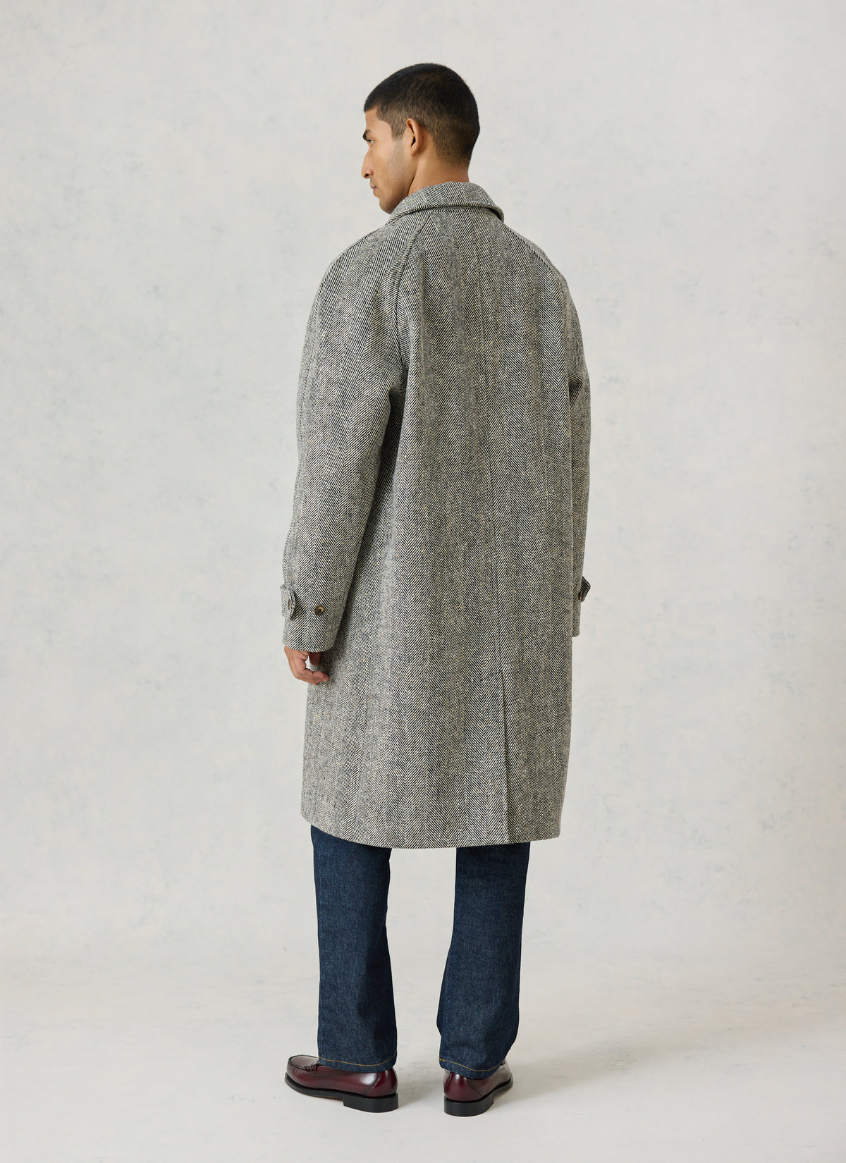 A model from the back wearing the Percival grey herringbone wool car coat, styled with blue jeans and dark shoes.
