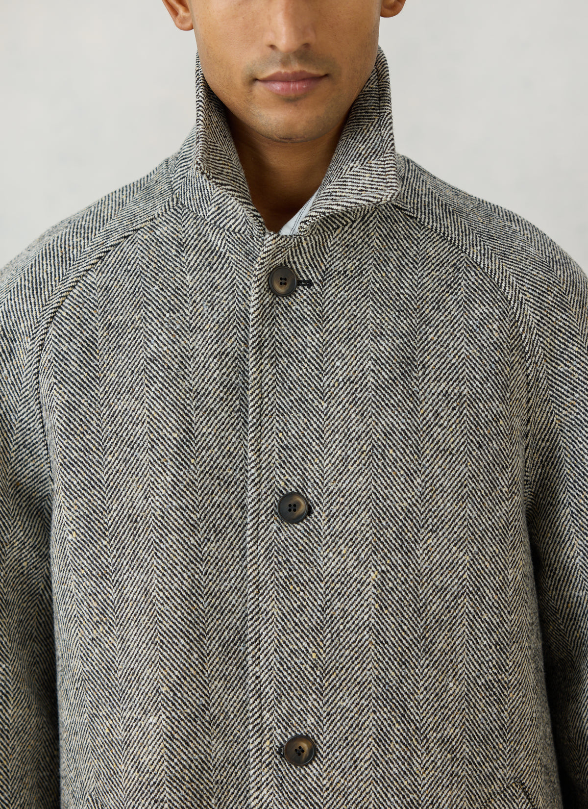 Close-up of a model wearing the Percival grey herringbone wool car coat, highlighting the collar and button-through front.