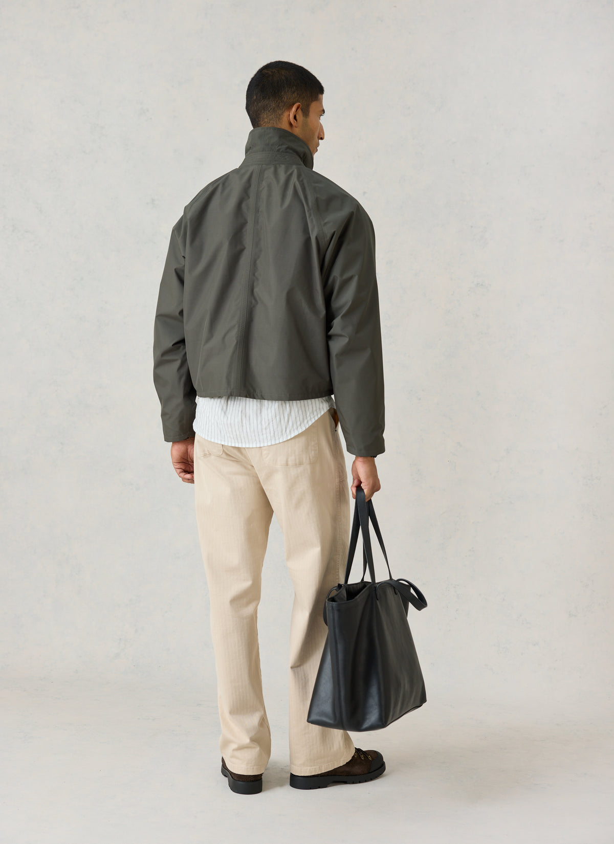 Model from the back wearing Percival's forest green Hunter Jacket, styled with beige trousers and carrying a black tote bag.