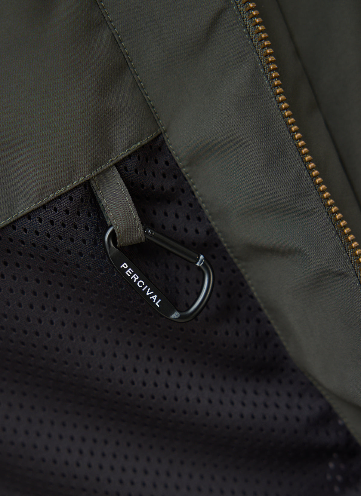 A close-up of the forest green Percival Hunter Jacket showing the black mesh pocket detail and branded carabiner.