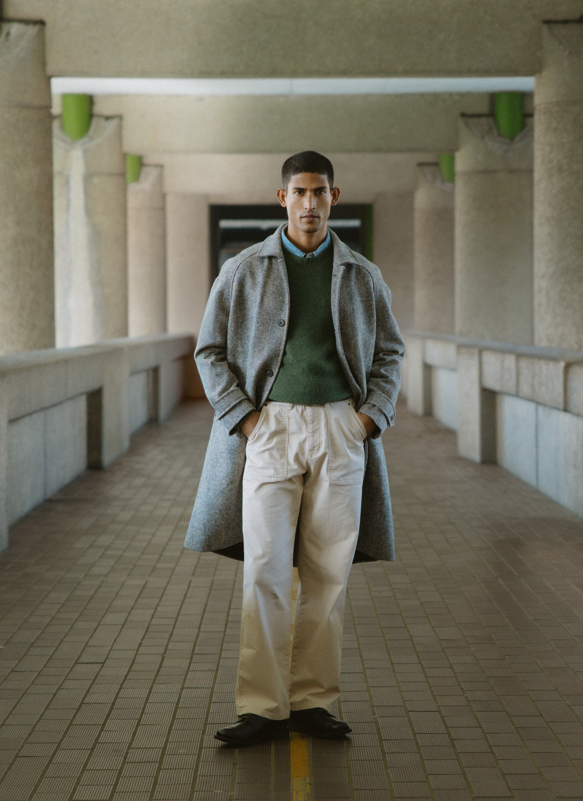 A model wearing the grey herringbone wool car coat by Percival, styled in an industrial concrete arcade.