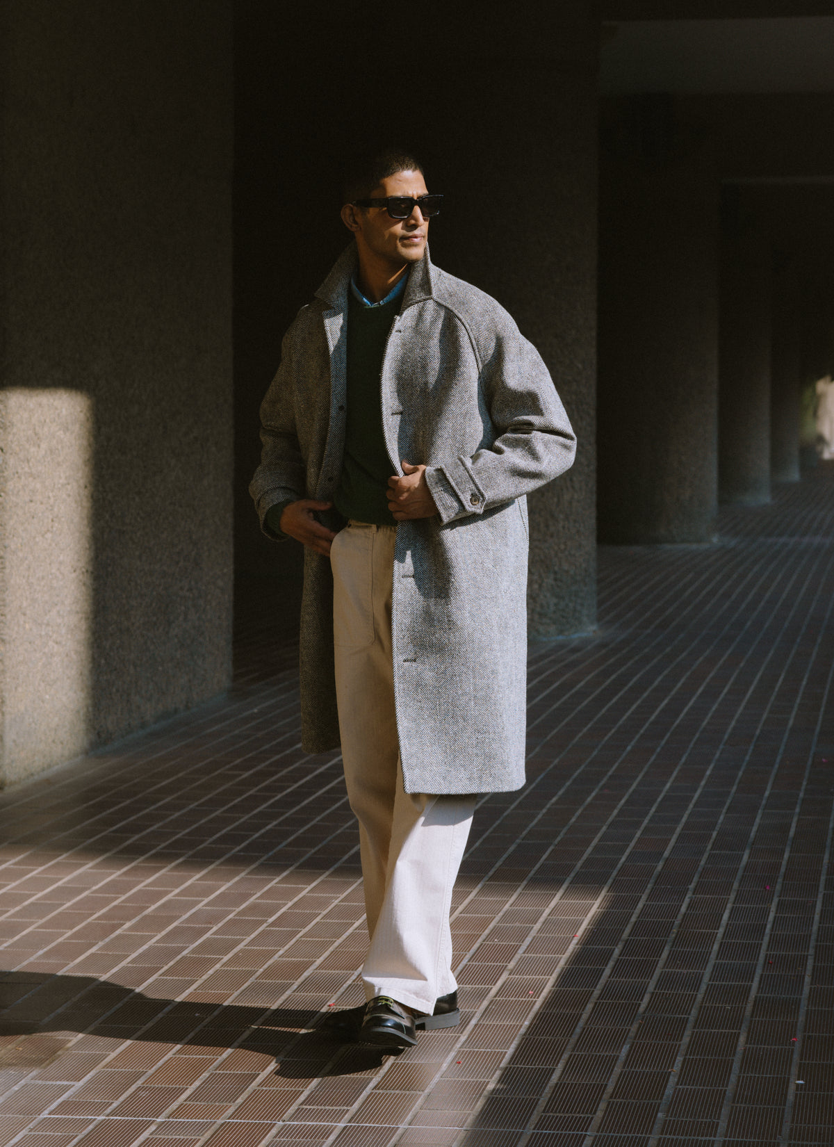 A model wearing the grey herringbone wool Percival car coat outdoors, featuring raglan sleeves and a buttoned front.