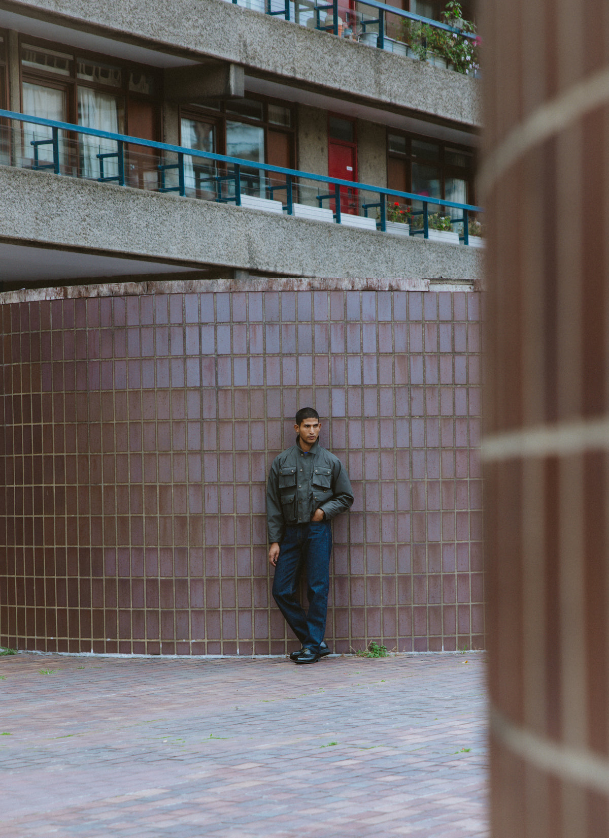 A model standing in front of a curved tiled wall wearing a dark hunter jacket and dark trousers.