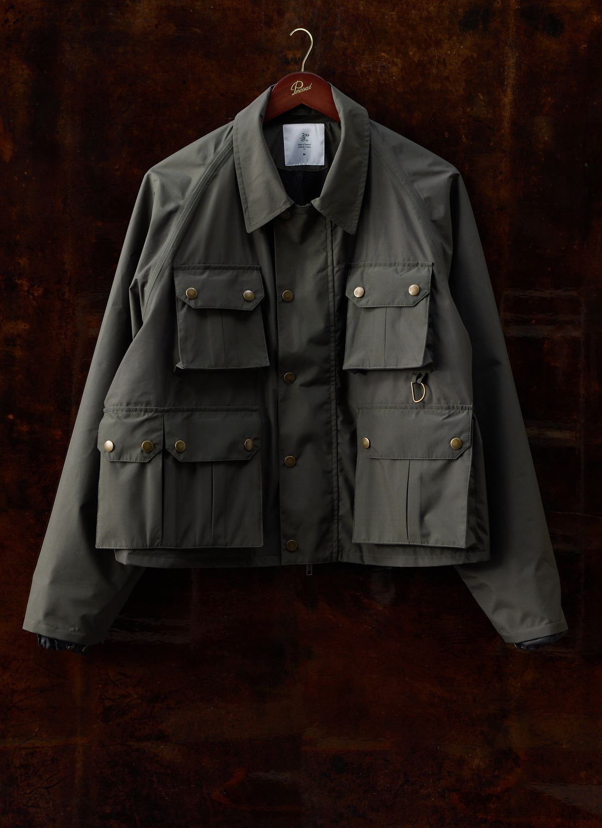 Forest green Percival Hunter field jacket hanging on a hanger, showing its four front flap pockets.