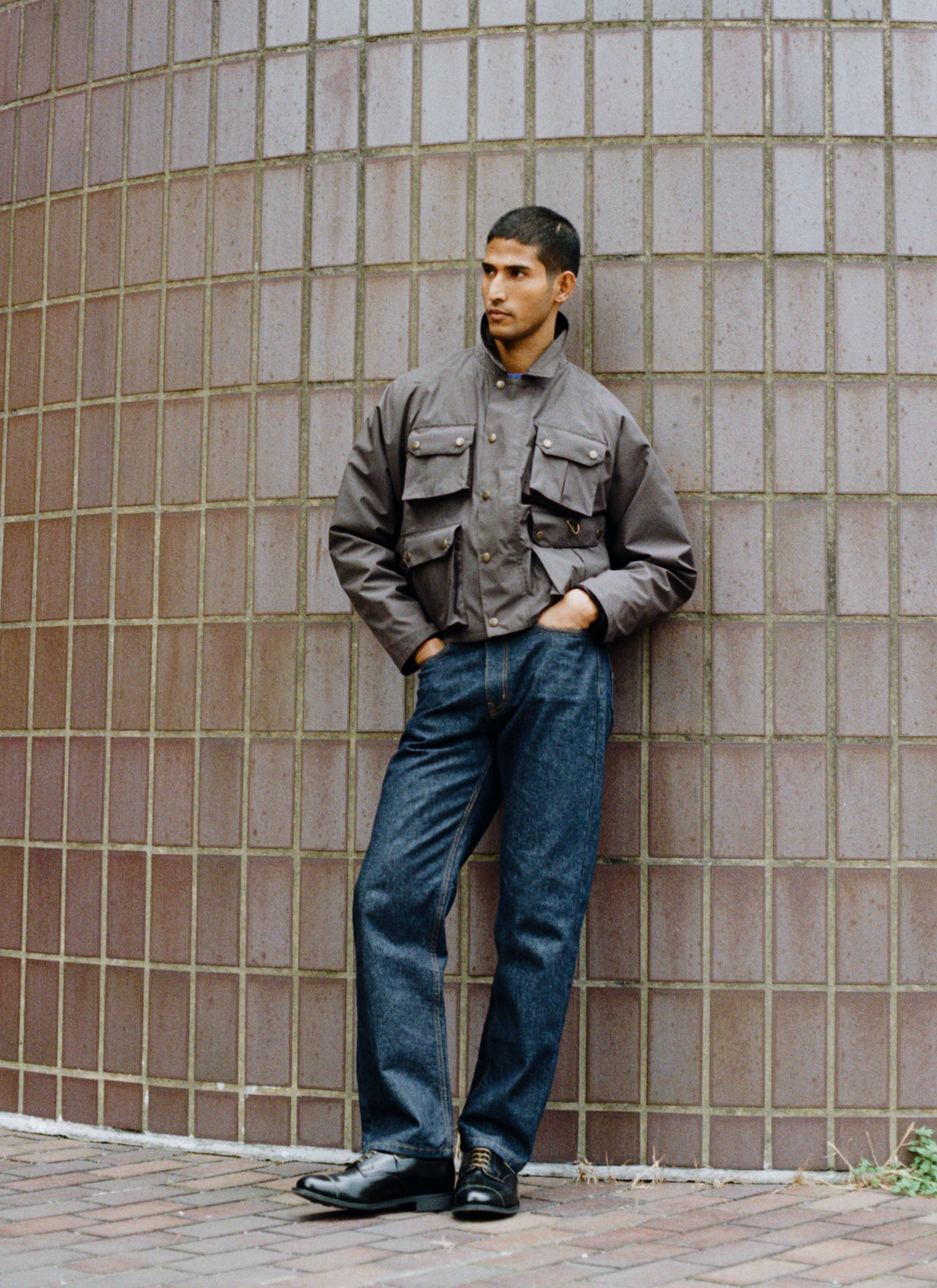 A model wearing Percival's forest green Hunter Field Jacket, paired with denim jeans and black shoes against a tiled wall.