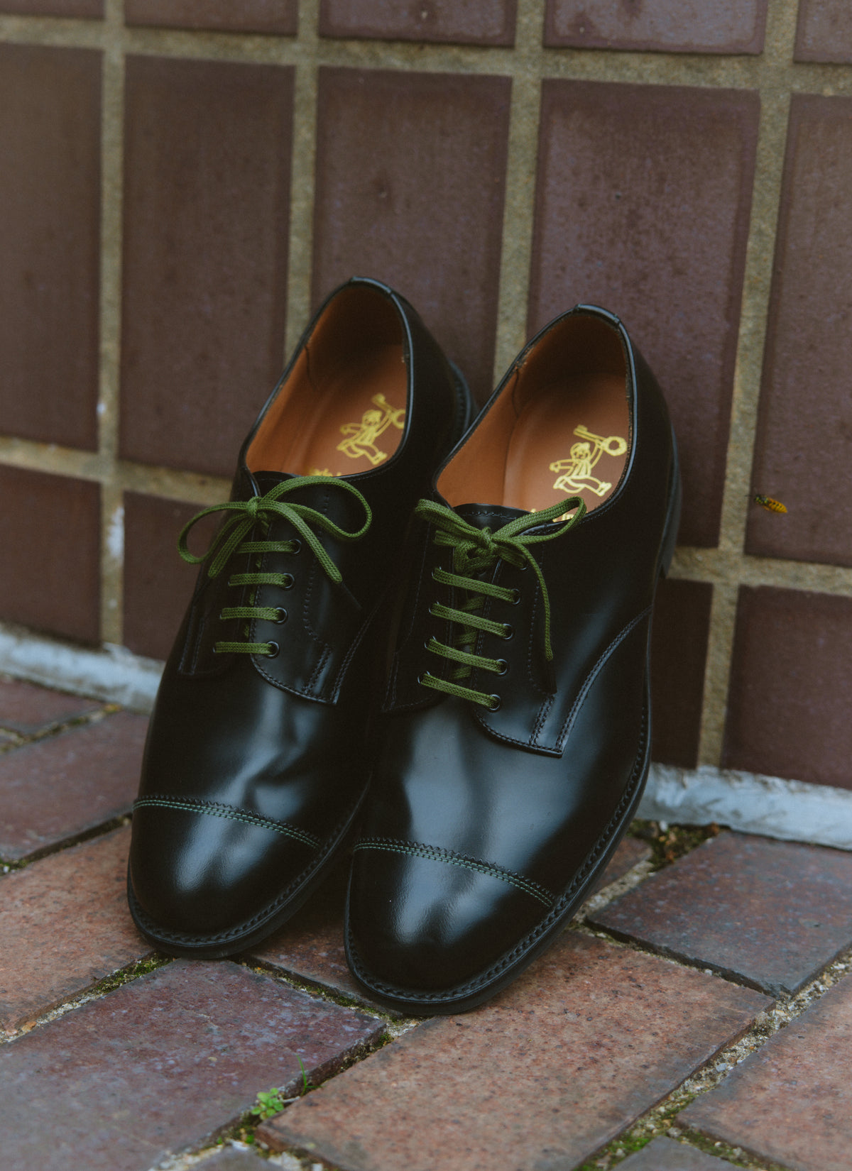 Black leather Derby shoes by Percival made in England, featuring contrast military green laces and gold branding inside.