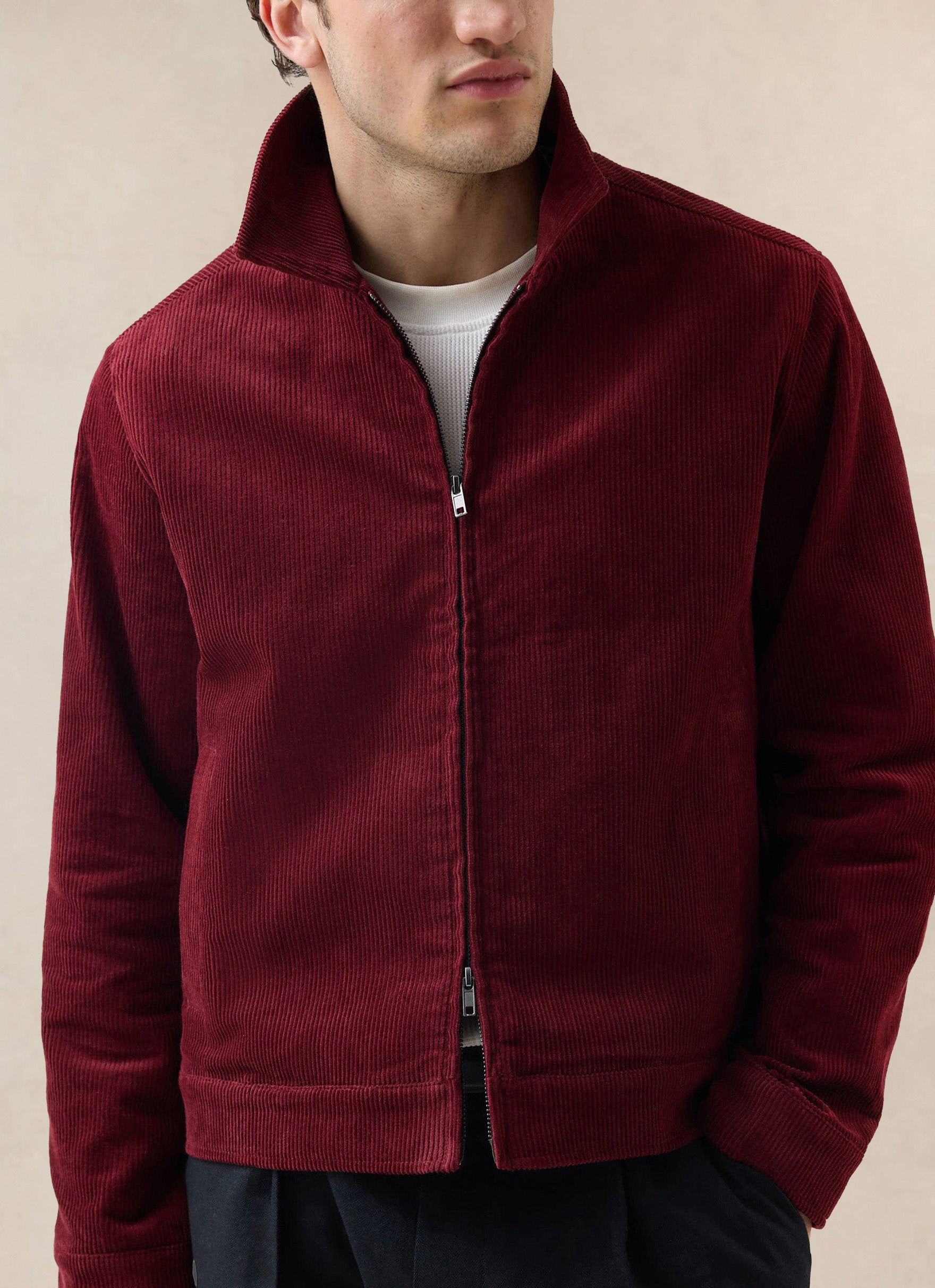 A close-up shot of a model wearing the burgundy Percival cord zip jacket over a white t-shirt.