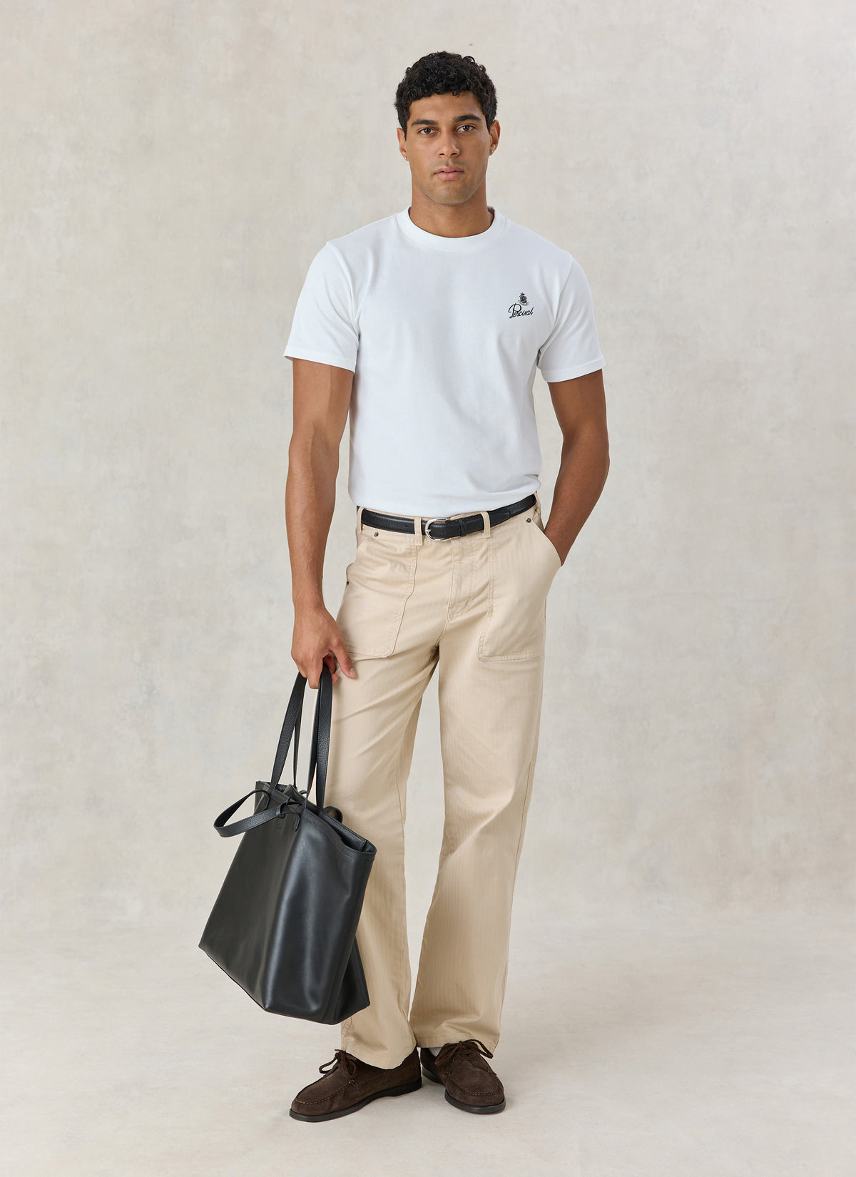 A model wearing the white Percival Martini Duo organic cotton T-shirt with beige trousers and a black leather tote bag.
