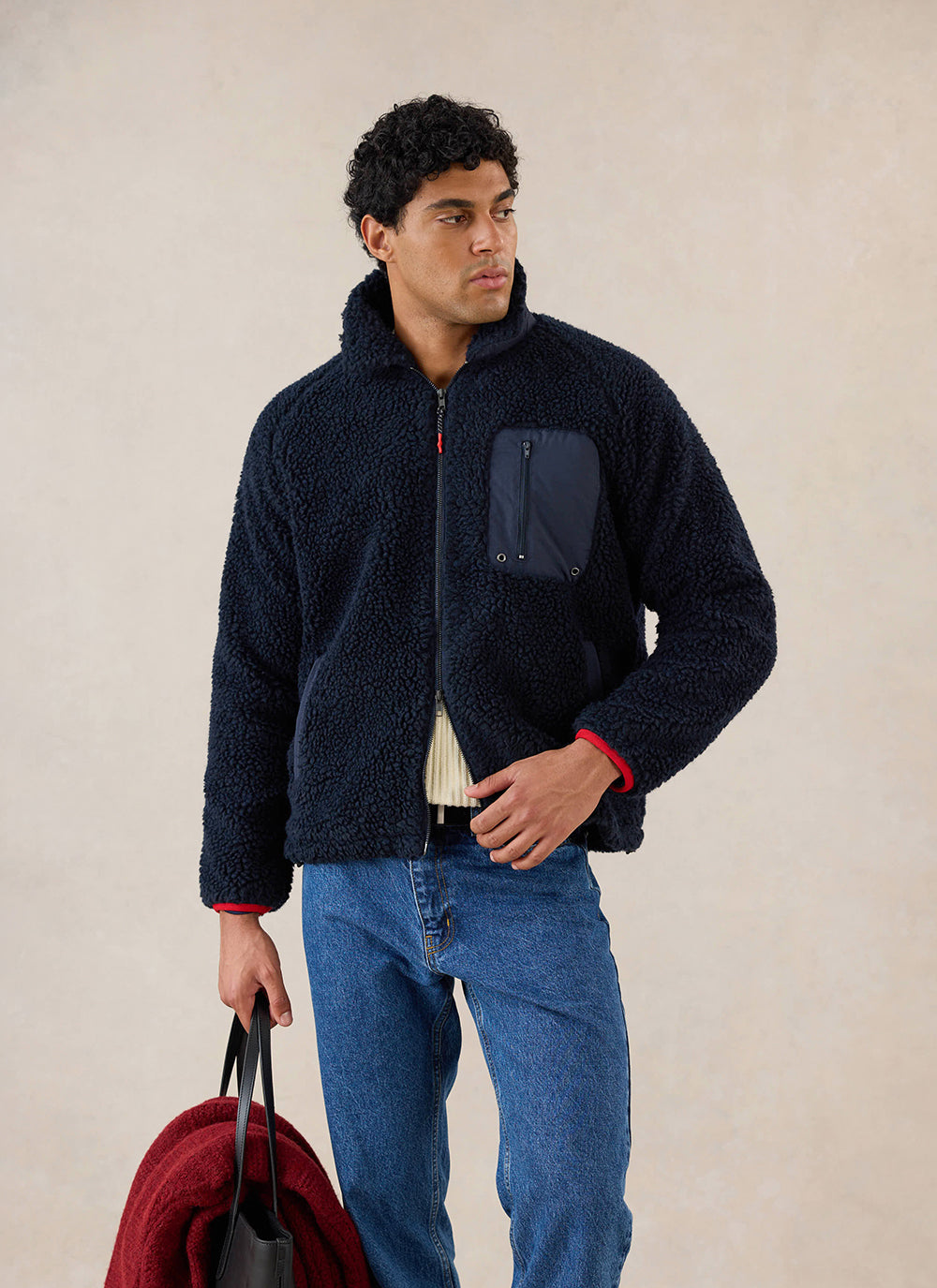 A model wears the navy Percival fleece jacket with a zippered chest pocket, styled with blue jeans and holding a red bag.