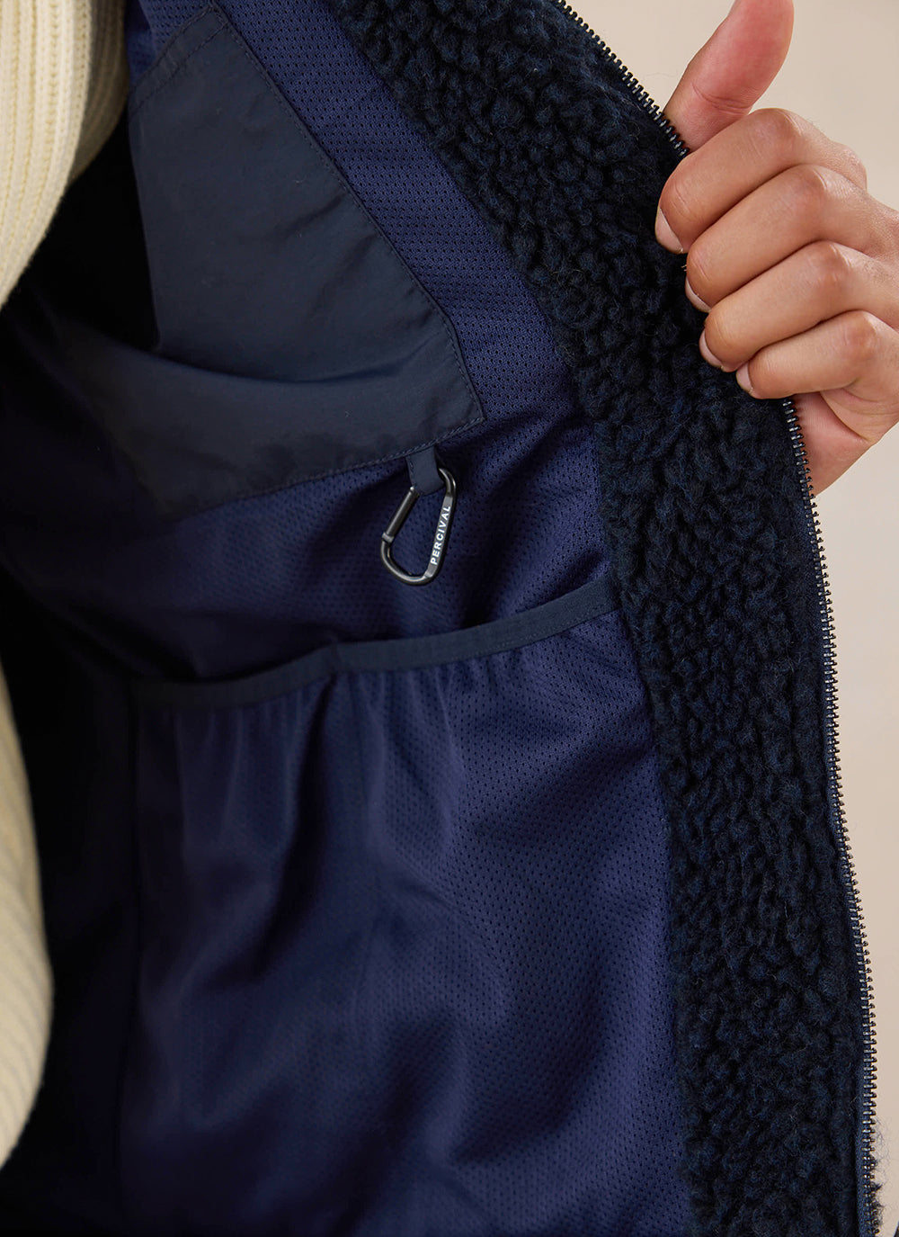 Close-up view of the interior lining, pocket detail, and carabiner of the navy wool fleece jacket from Percival.