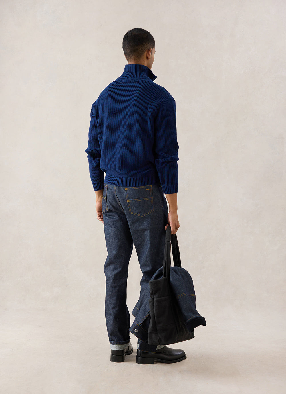 Rear-view studio shot of a model wearing the navy Percival Meyer Boxy Quarter Zip, styled with dark trousers and a tote bag.