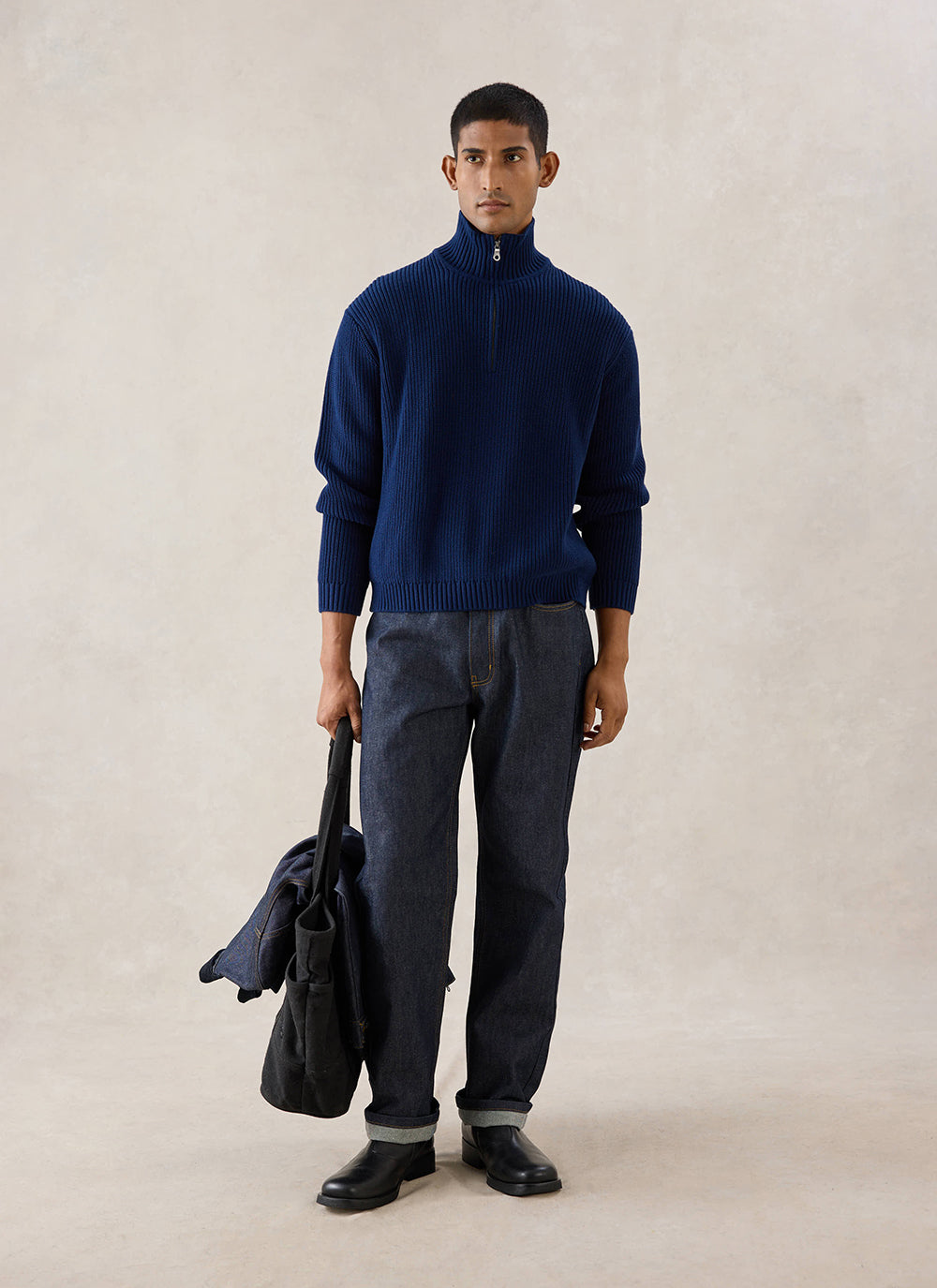 A model wears the navy Percival Meyer boxy quarter zip, styled with dark trousers and holding a bag in a studio.