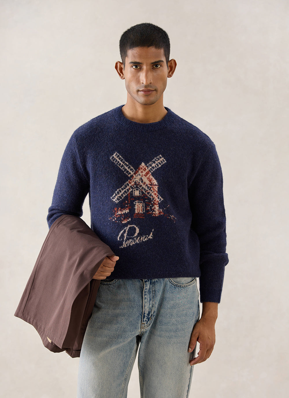 A model wears the navy Miller jacquard jumper from Percival featuring a windmill design, styled with light blue jeans.